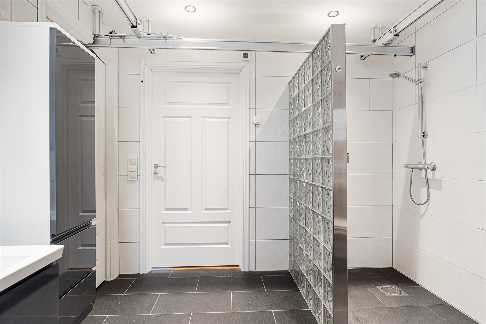 Badet er innredet med moderne baderomsinnredning, dusjvegg i glassbyggerstein samt vegghengt toalett med dusj og føn - badet er i også utstyrt med takheis fra hjelpemiddelsentralen (se mer info om takheis i salgsoppgaven) Galleribilde