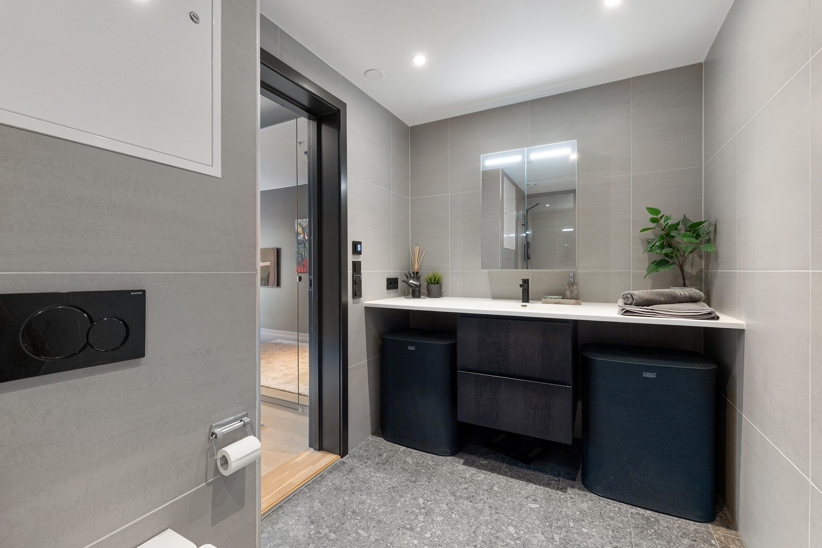 Badet er innredet med stilren baderomsinnredning med skuffer og vegg-til-vegg benkeplate i komposittstein med helstøpt servant, samt toalett og badekar med innfellbar dusjvegg. Galleribilde