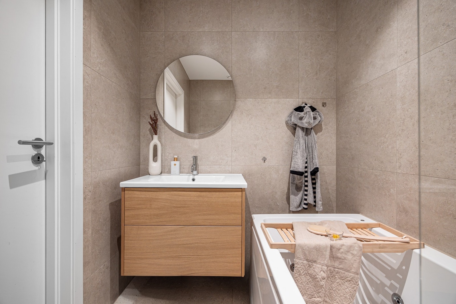 Badet er romslig og delikat med store vegg- og gulvfliser i beige toner, downlights og elektriske varmekabler. Galleribilde