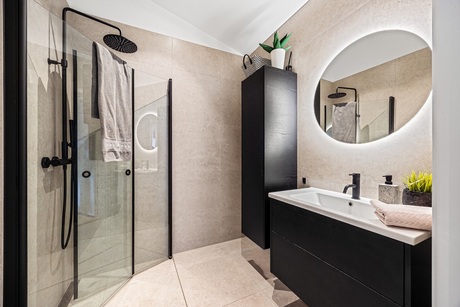 Badet har et stilrent uttrykk med store vegg- og gulvfliser i beige toner som gir et tidløst uttrykk. Galleribilde