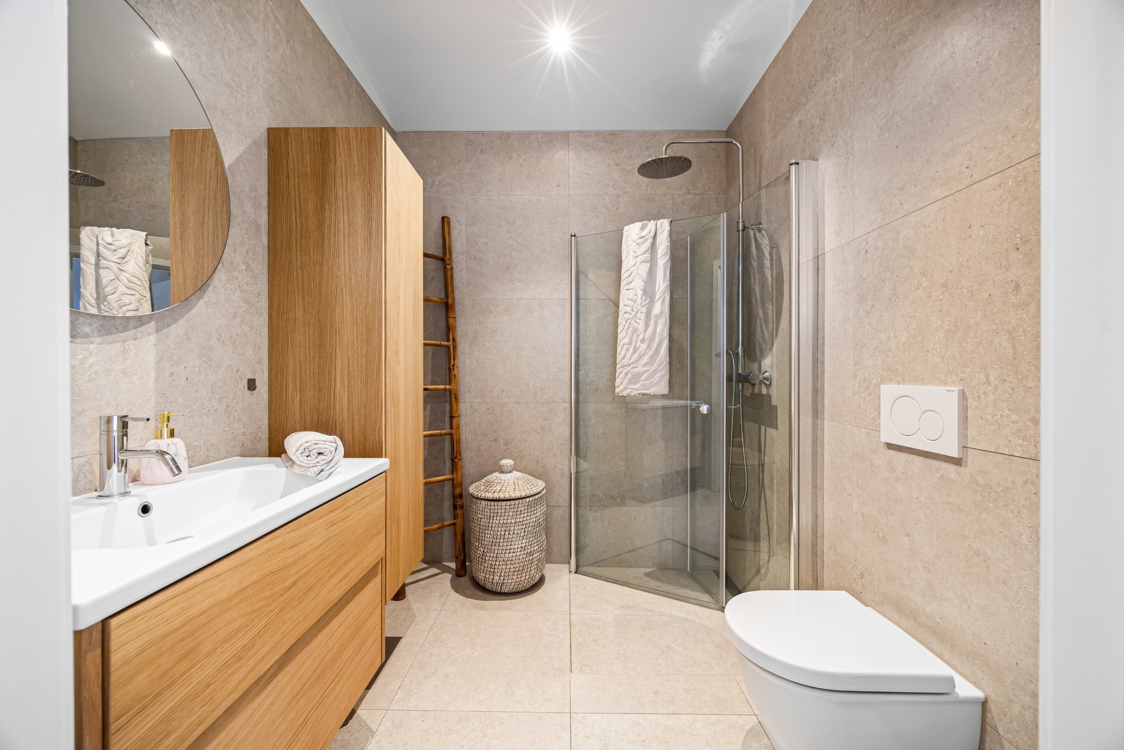 Badet har et stilrent uttrykk med store vegg- og gulvfliser i beige toner som gir et tidløst uttrykk. Galleribilde