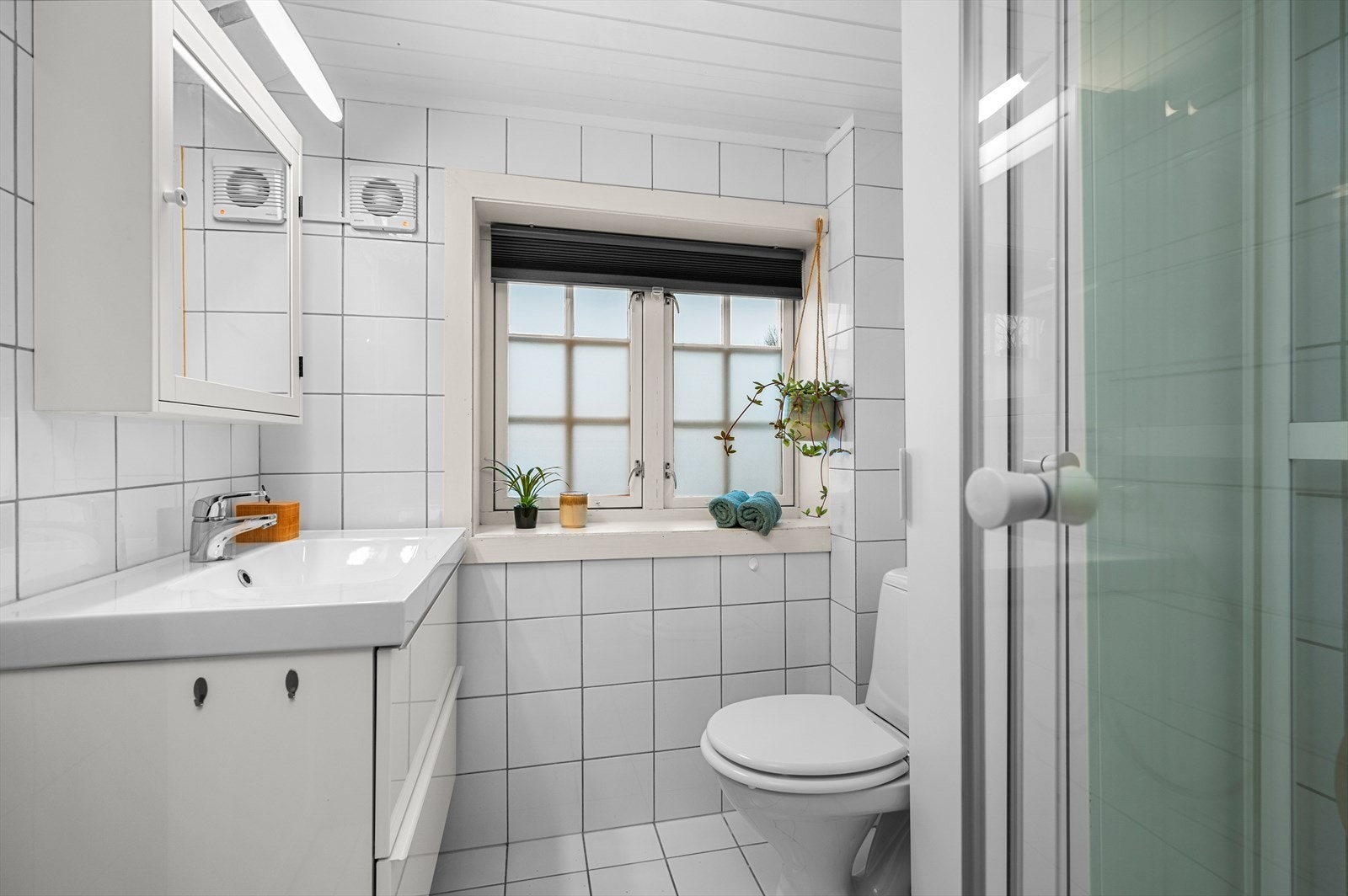 Lyst og flislagt bad med dusj, toalett og servant i skap. Galleribilde