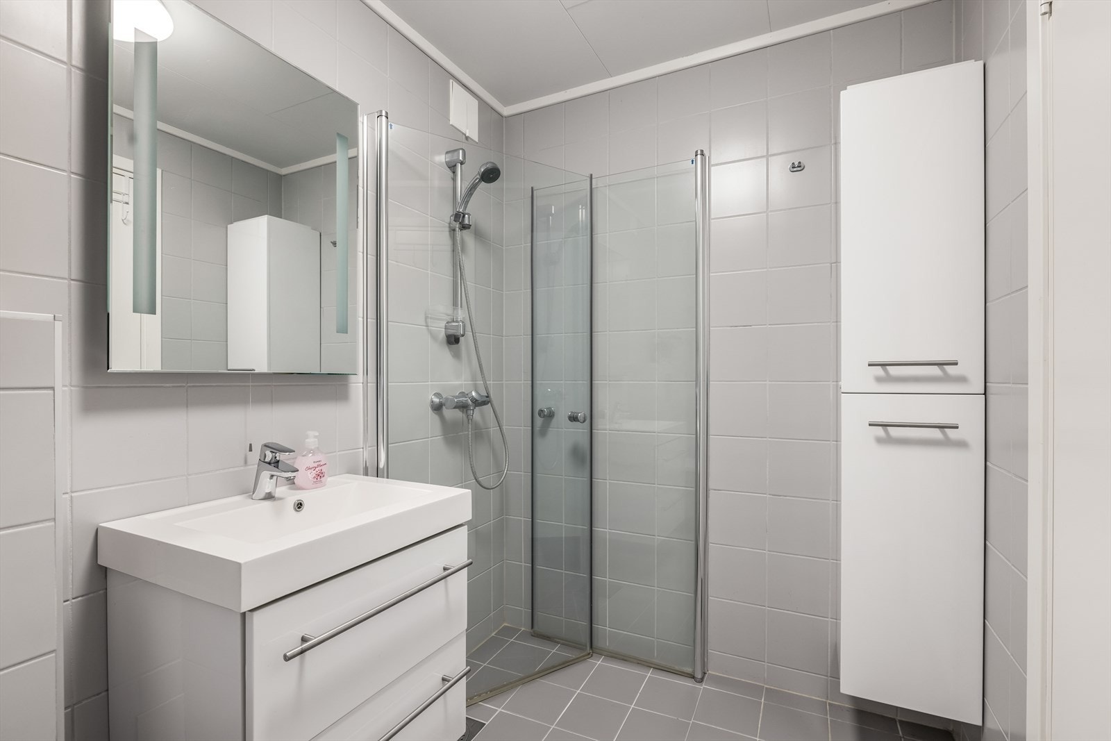 Badet er utstyrt med dusjhjørne med glassvegger, servant med underskap, speilskap og vegghengt toalett. Galleribilde