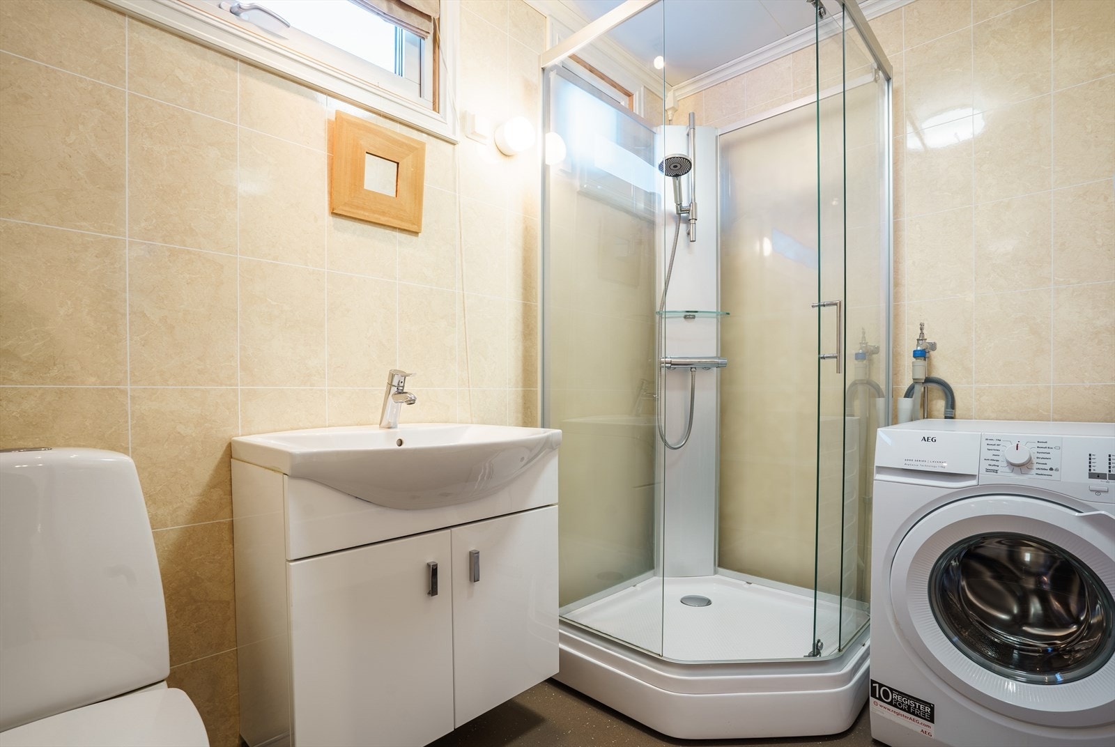 Lyst og moderne bad med dusjkabinett, vaskemaskin og stilren servant. Perfekt for en praktisk og komfortabel hverdag. Galleribilde