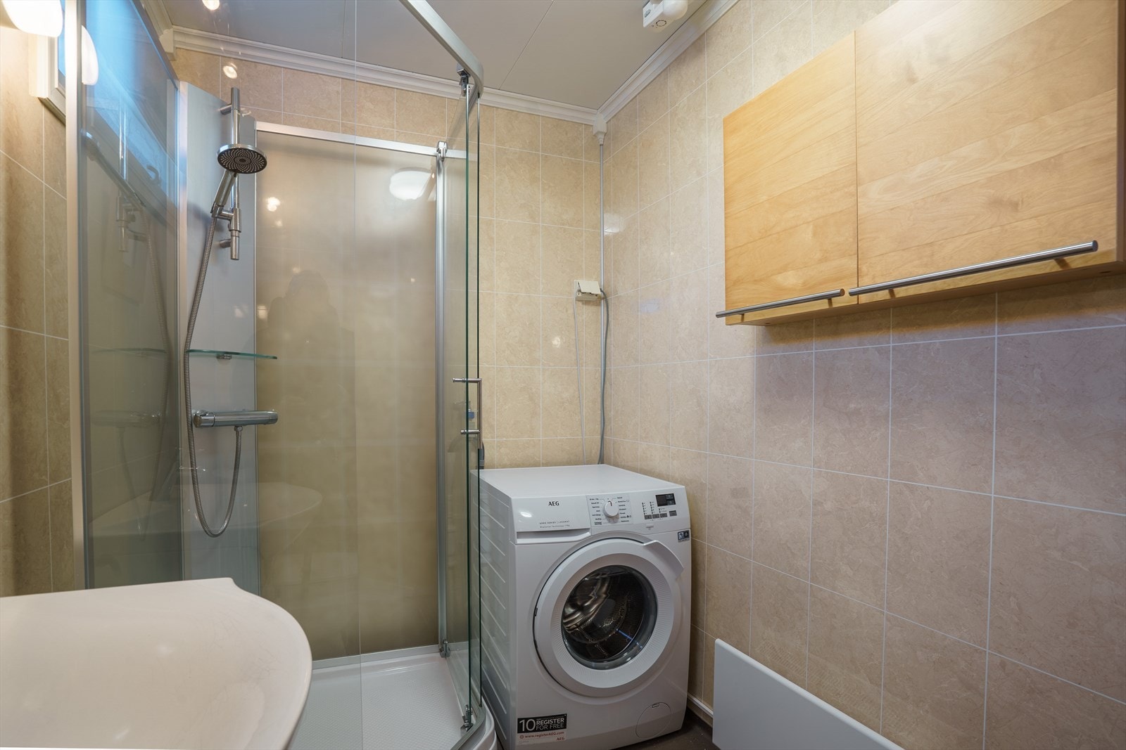 Moderne bad med dusjkabinett, vaskemaskin og praktisk oppbevaring. Baderomsplatene gir et stilrent og lettstelt inntrykk. Galleribilde