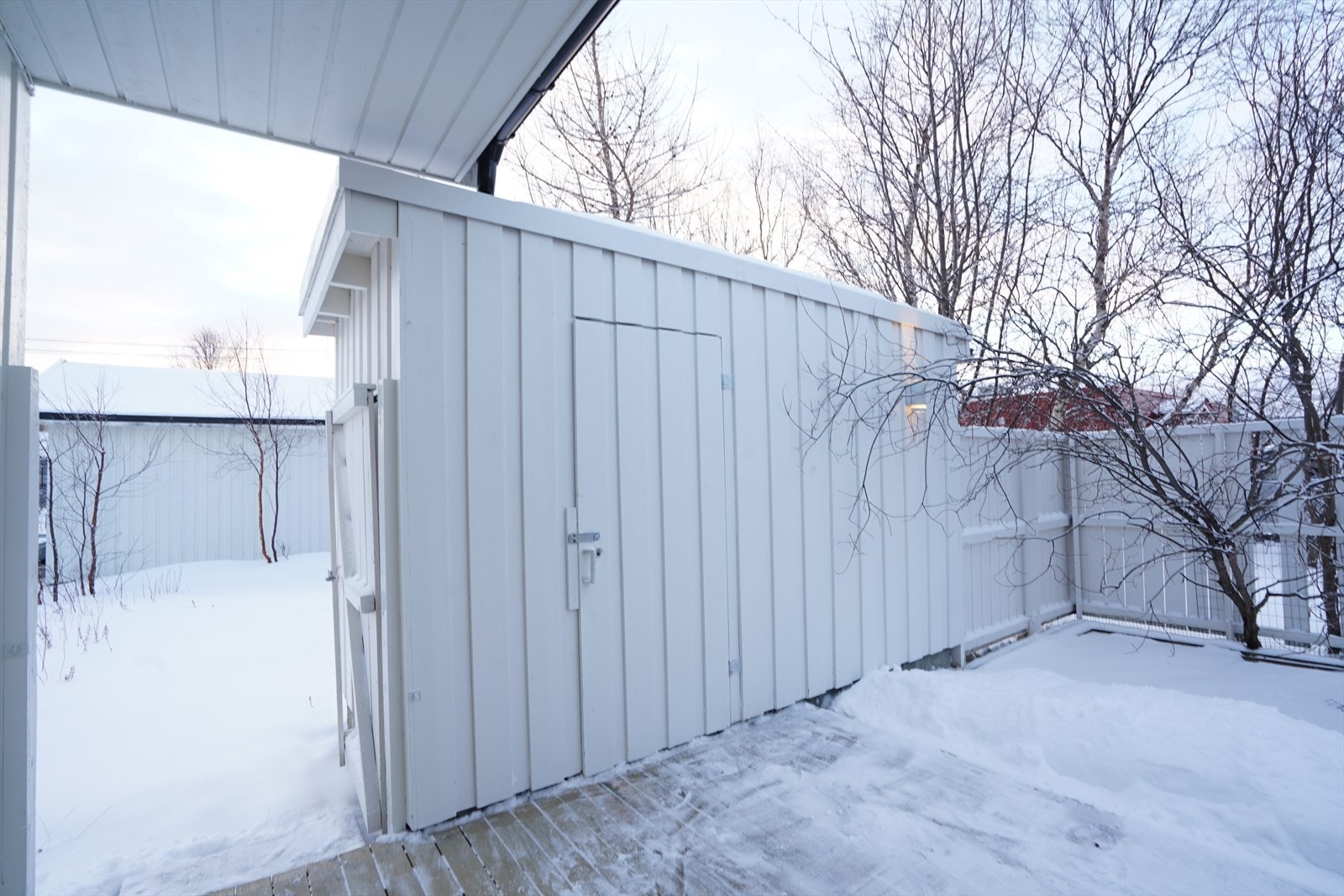 Moderne uteområde med hvitt gjerde og bod, omkranset av snødekte trær. Perfekt for vinterhygge i naturskjønne omgivelser. Galleribilde