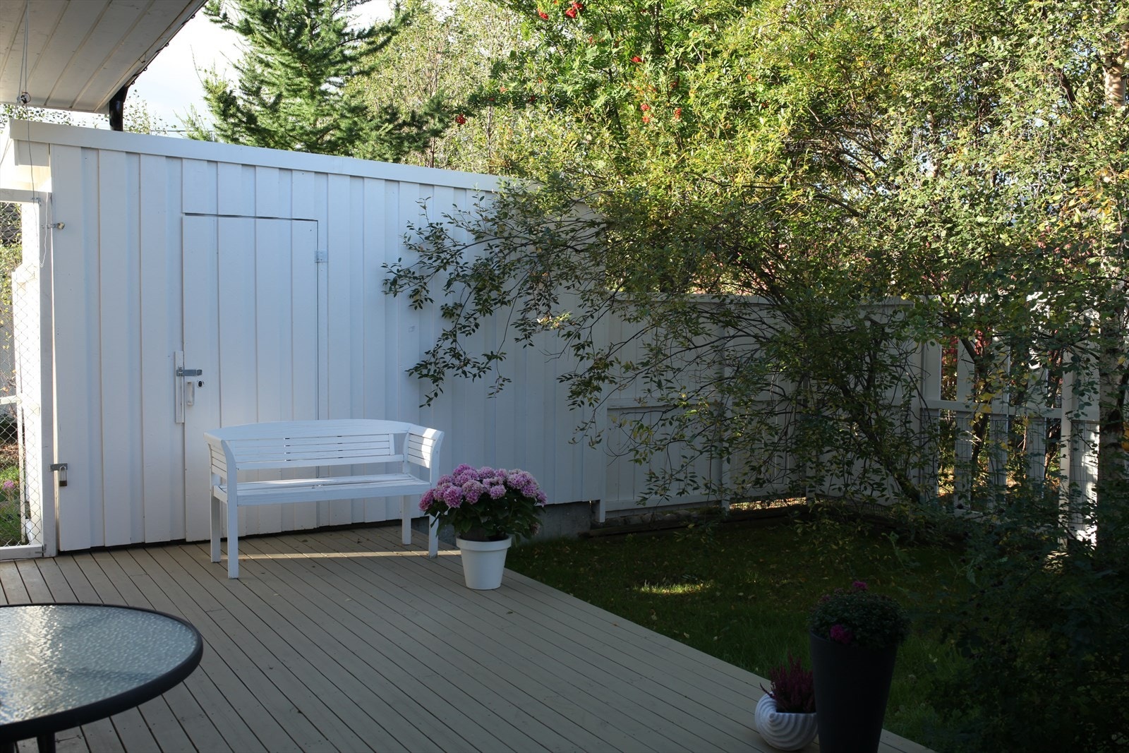 Koselig uteplass med hvitt gjerde, benk og frodig vegetasjon. Perfekt for avslapning i solfylte omgivelser. Galleribilde