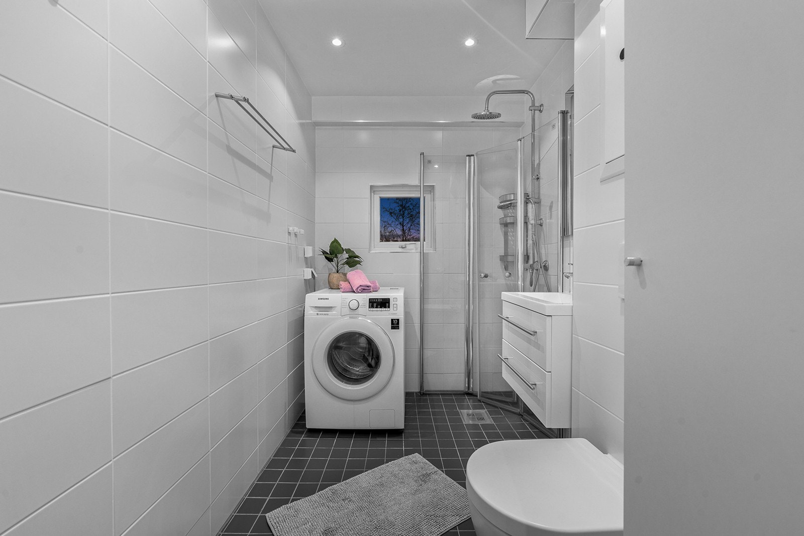 Badet har dusjhjørne med dusjdører i herdet glass, heldekkende servant med underskap samt speil med integrert belysning. Videre er det vegghengt toalett, baderomsskap og opplegg samt avsatt plass til vaskemaskin Galleribilde