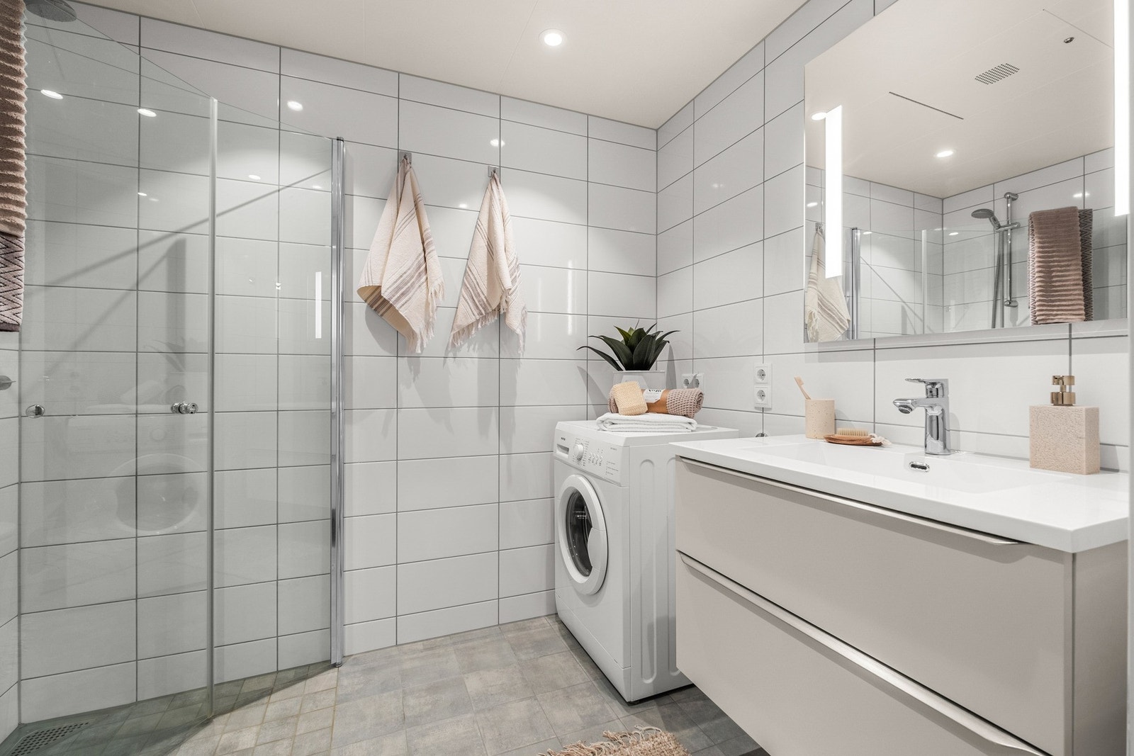 Pent flislagt bad med dusjhjørne, vegghengt WC, servantskap m/skuffer og opplegg til vaskemaskin. Galleribilde