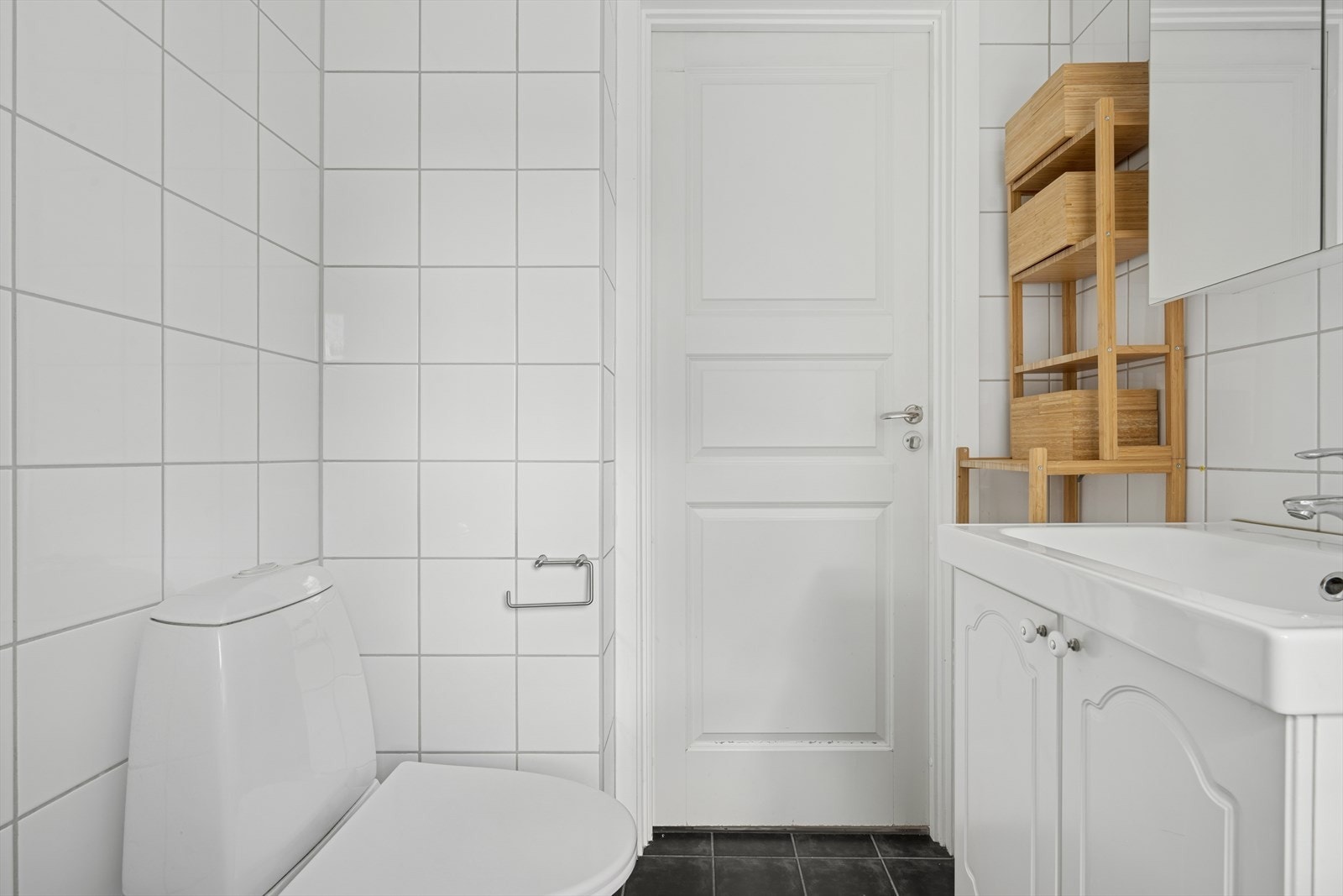 Baderommet er innredet med gulvmontert toalett, servant, åpen dusjsone med dusjgarnityr på vegg. Opplegg for vaskemaskin. Galleribilde