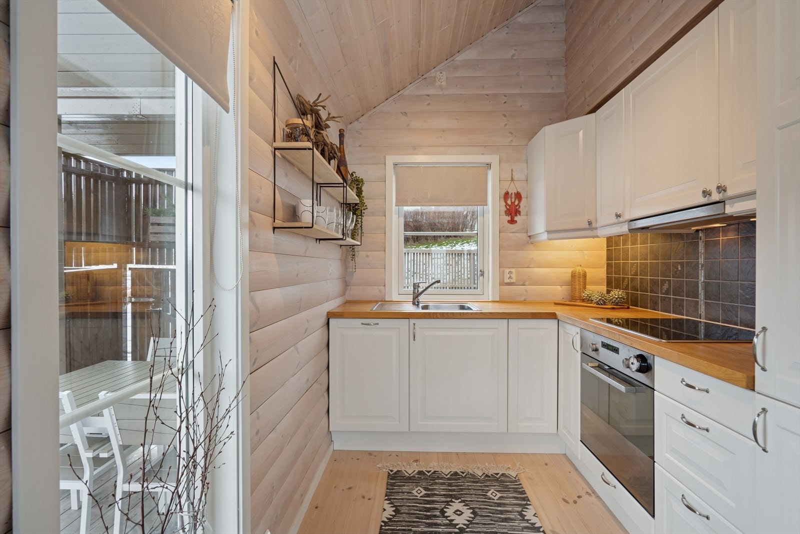 Kjøkkenet er utstyrt med hvite profilerte fronter og fliser over stekesonen og hvitevarer som stekeovn, platetopp, oppvaskmaskin og kombinert kjøl-/fryseskap. Galleribilde