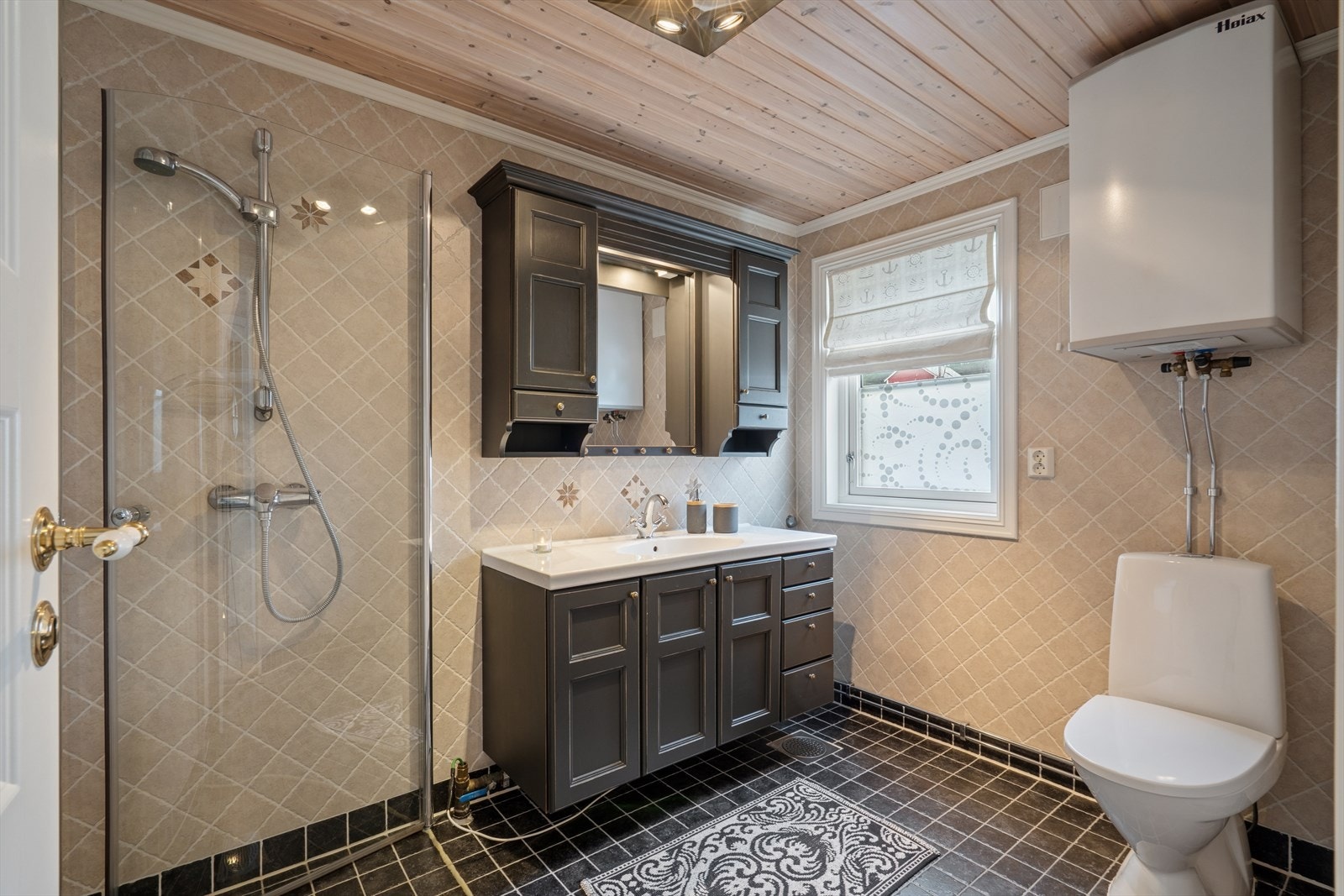 Baderommet er av god størrelse og innredet med fliser på både gulv og vegger, samt panel i himlingen. Rommet er utstyrt med nedfelt servant i innredning med speil og belysning, sideskap, toalett og dusj med innfellbare dører. Galleribilde