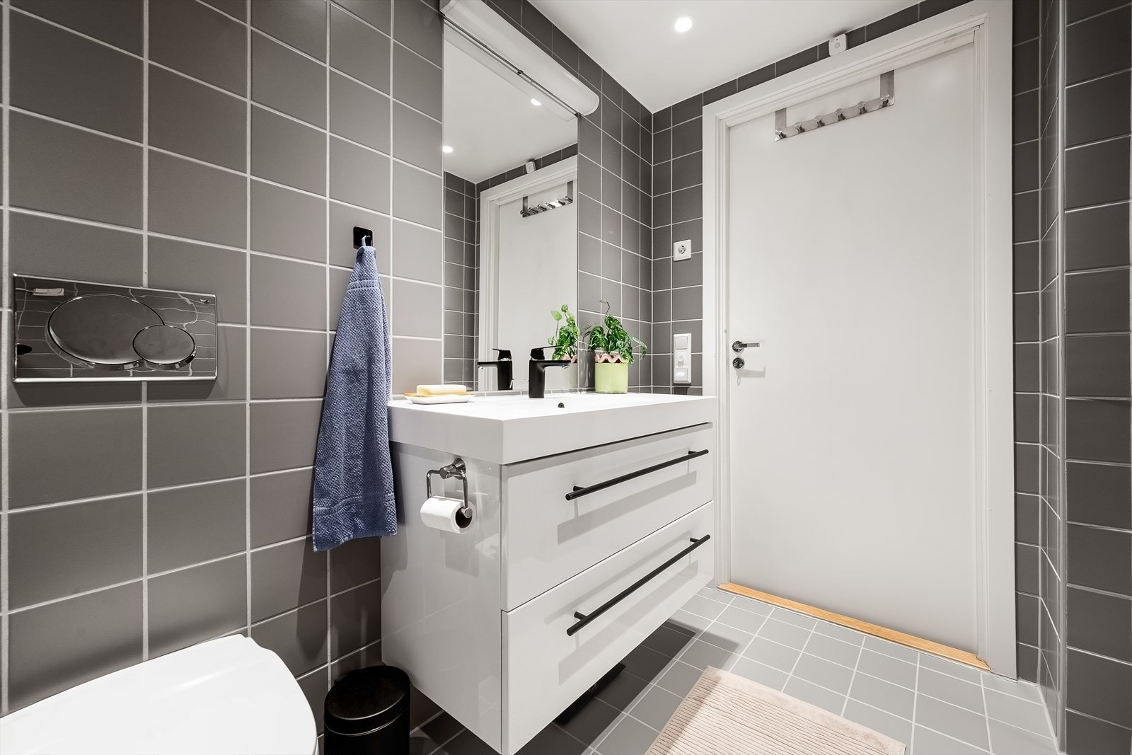 Badet er utstyrt med vegghengt toalett, dusjhjørne med svingbare glassdører og baderomsinnredning fra Blum med skuffer, nedfelt servant og speil med belysning. Det er opplegg for vaskemaskin. Galleribilde