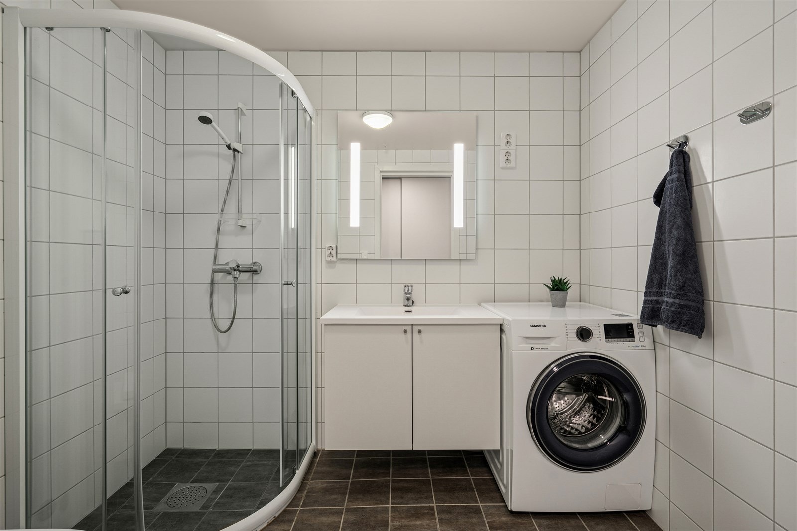 Det helflisede badet er innredet med en servant nedfelt i baderomsinnredning, veggmontert toalett og et dusjhjørne med dusjvegger. Galleribilde