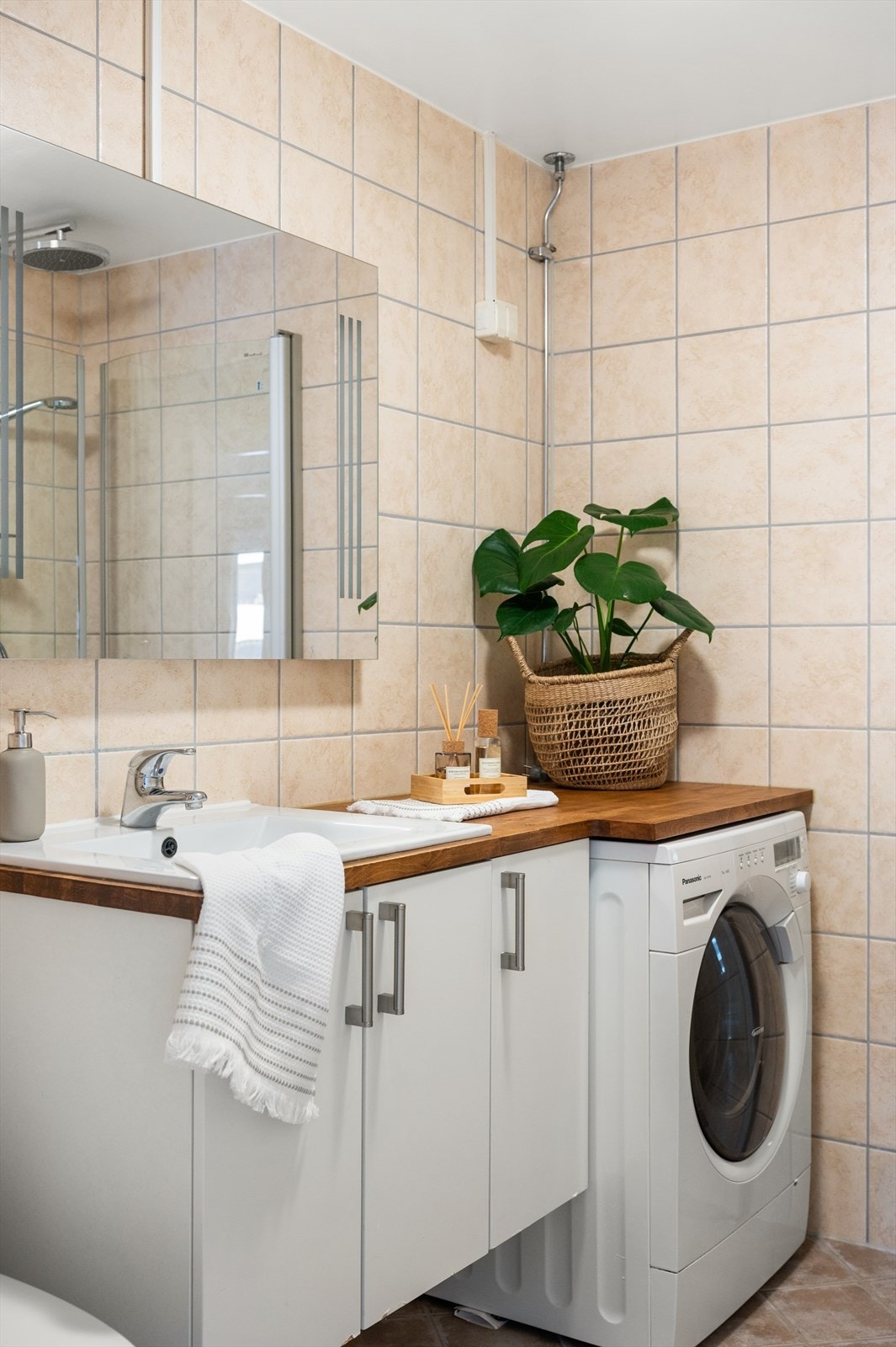 Badet inneholder gulvstående toalett, servant på vegghengt servantskap med speil og lys over. Dusjhjørne med vegghengte dursjører. Galleribilde