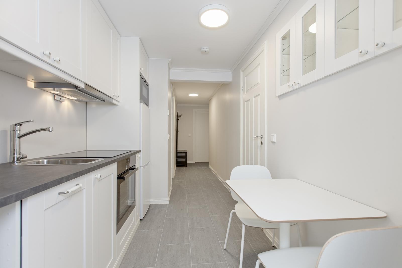 Lyst og pent kjøkken med integrerte hvitevarer, god skap- og benkeplass og sittegruppe Galleribilde