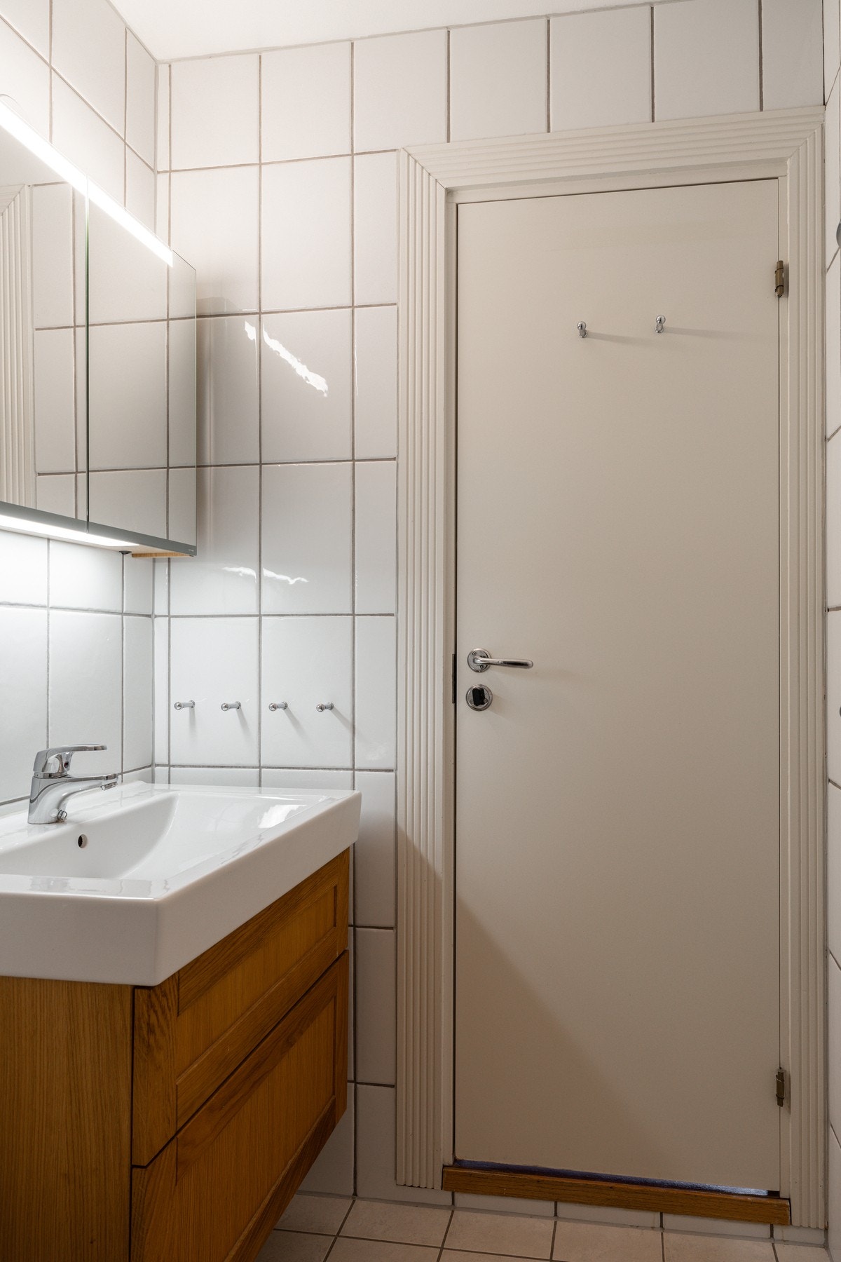 Flislagt bad innredet med dusjnisje med glassdører, gulvmontert toalett og baderomsinnredning med nedsunket servant og speilskap. Galleribilde