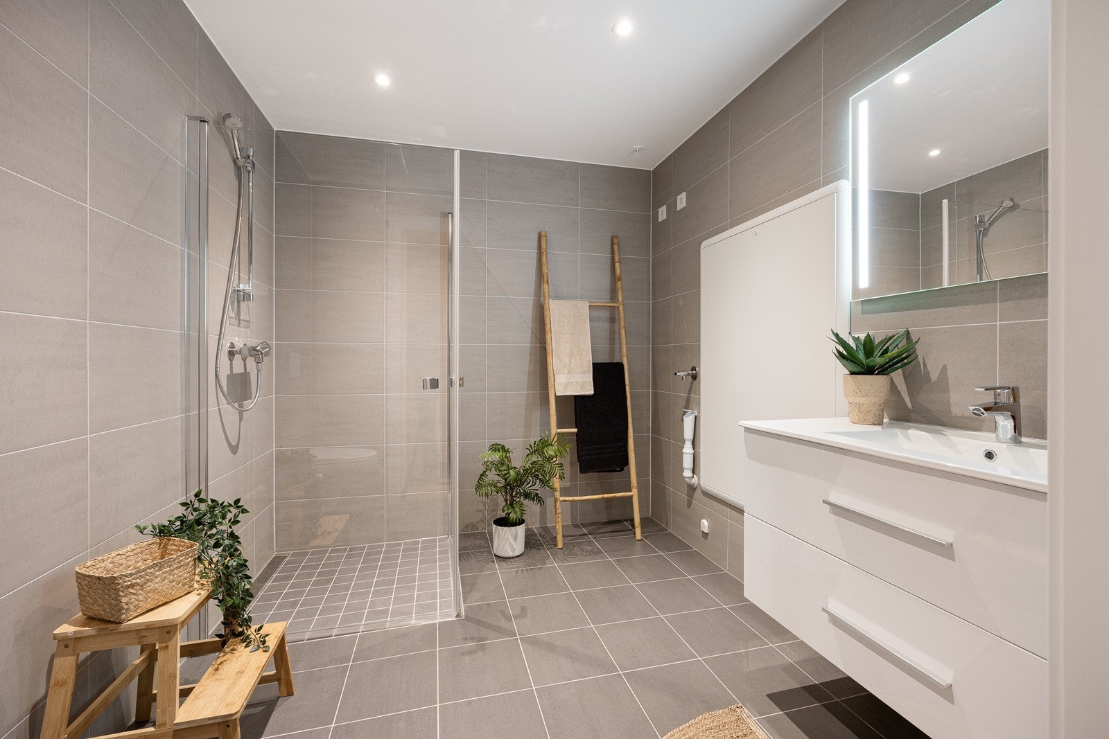 Badet er delikat utformet med grå fliser på gulv og vegger, gulvvarme og downlights Galleribilde