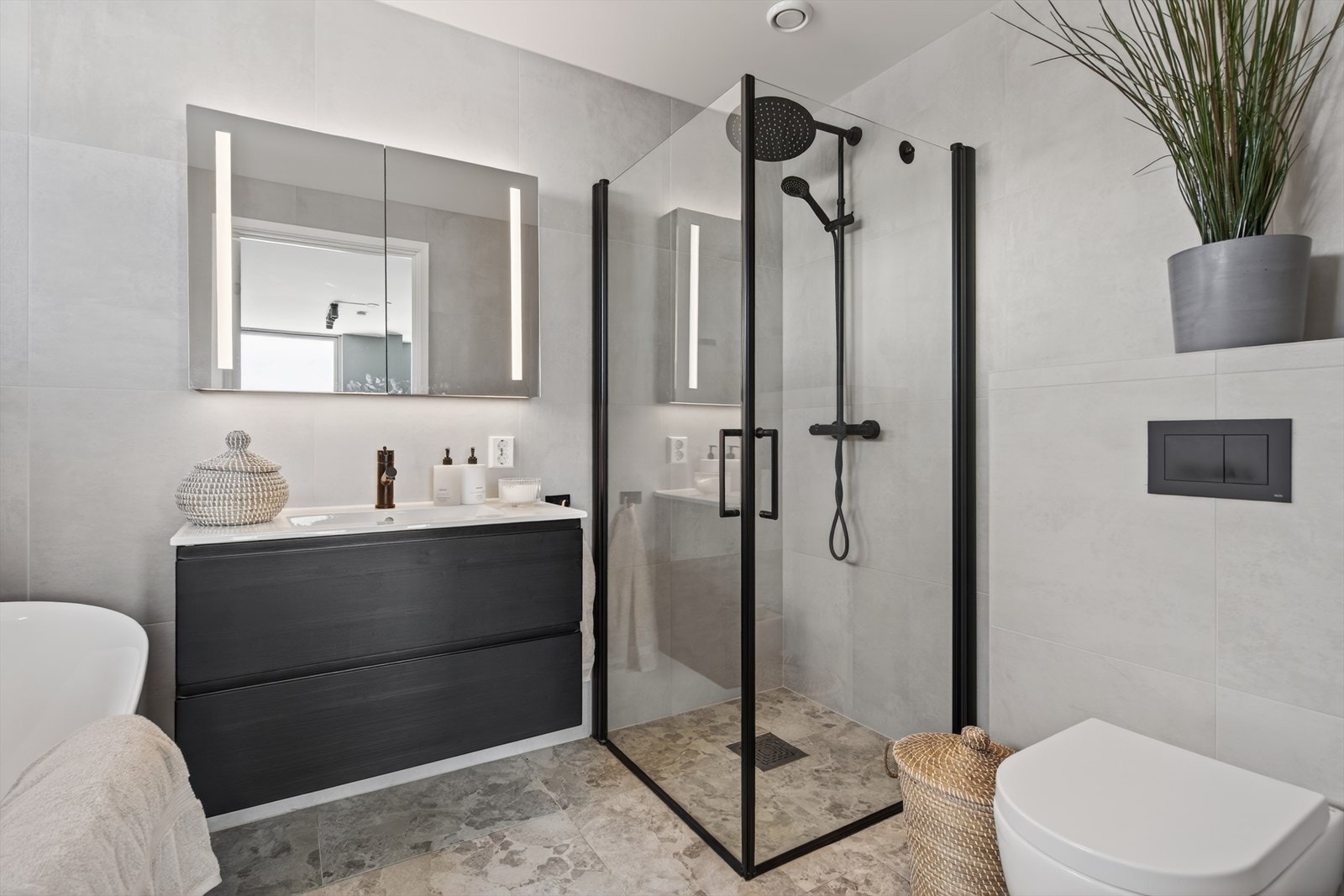 Rommet er innredet med dusjhjørne, badekar, veggmontert toalett og baderomsmøbel med heldekkende servant. Galleribilde