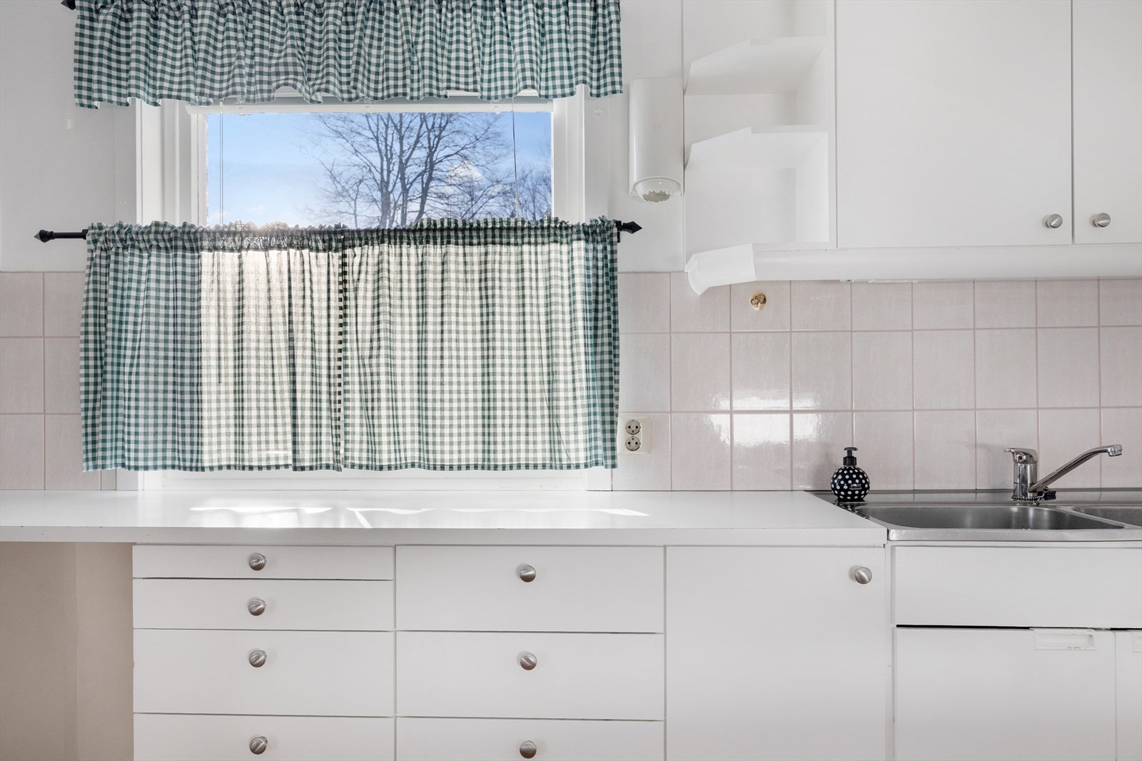 Kjøkkenet har innredning med hvite fronter og benkeplater i stål med nedfelt kum. Fliser er montert mellom overskap og underskap Galleribilde