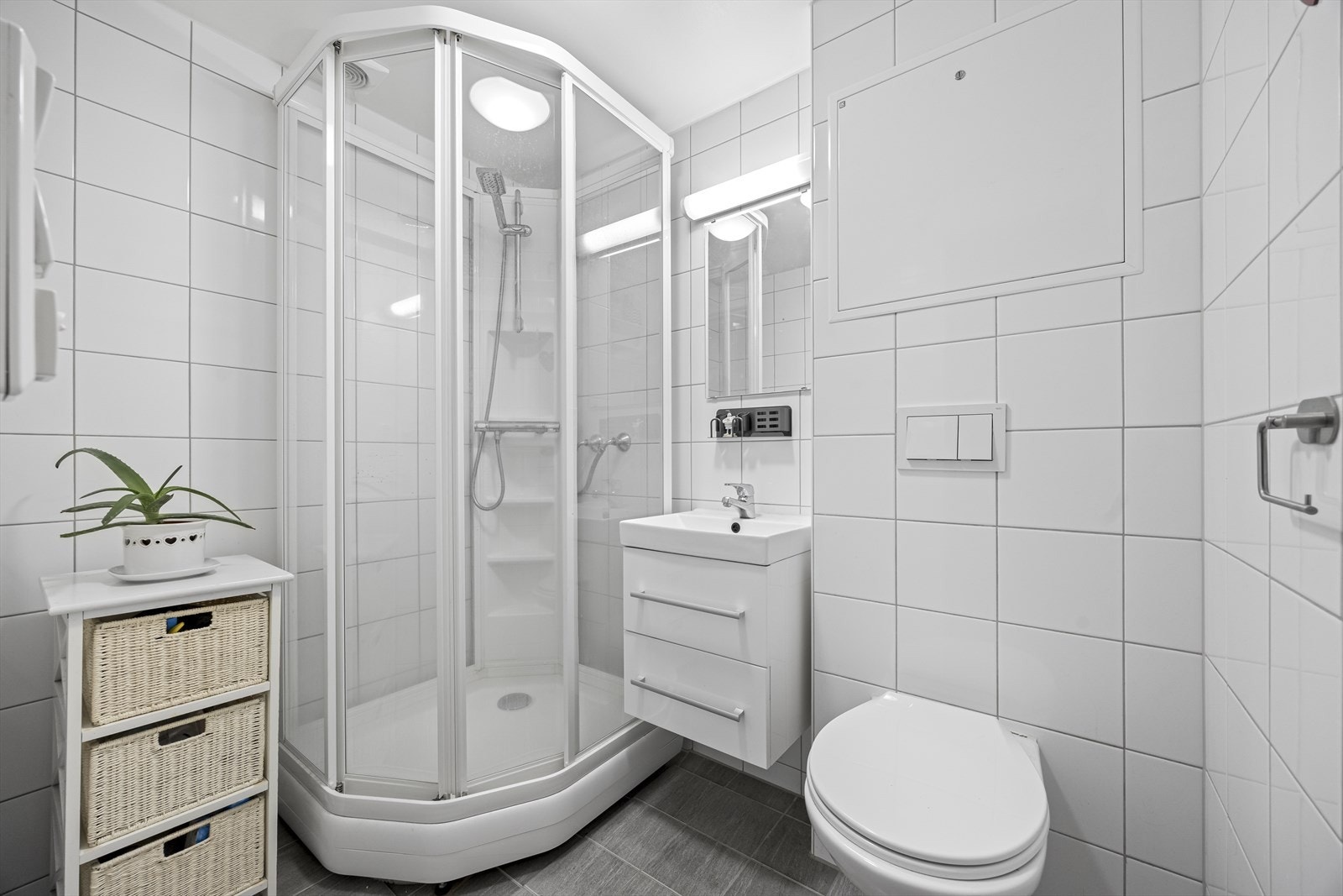 Badet er fliselagt med varmekabler i gulv, vegghengt toalett, servantinnredning med speil og dusjkabinett. Galleribilde