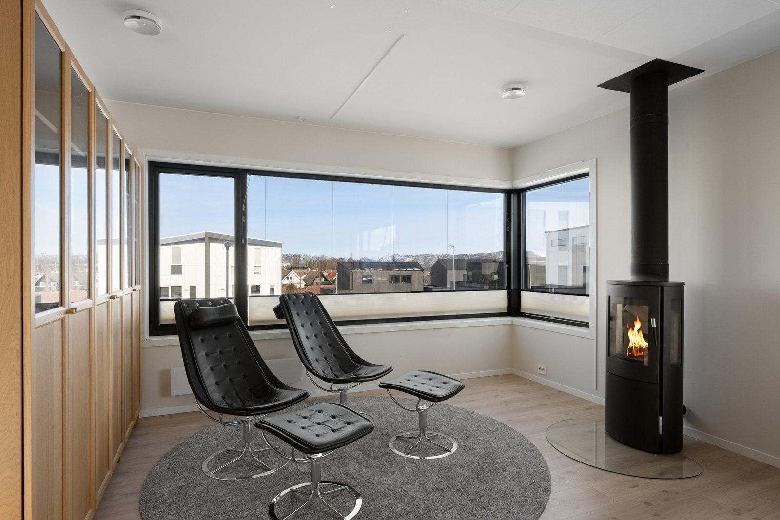 Åpen og romslig stue med store vinduer som slipper inn dagslys Galleribilde