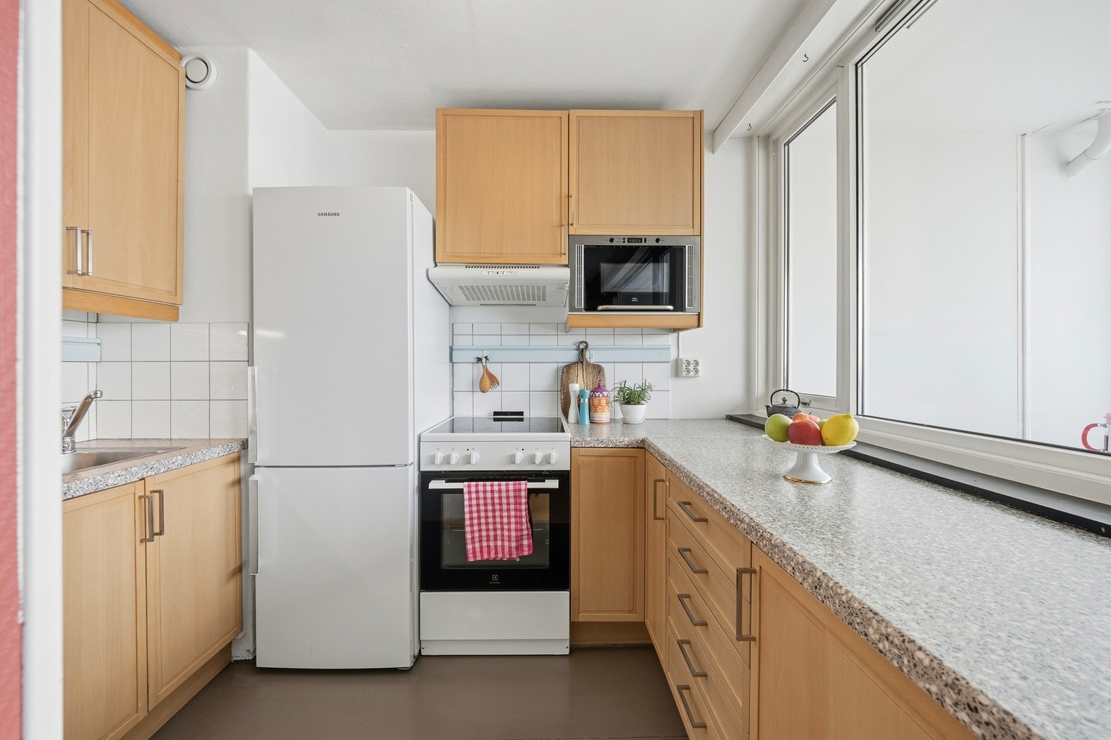 Leilighetens kjøkken har profilerte fronter og frittstående hvitevarer Galleribilde