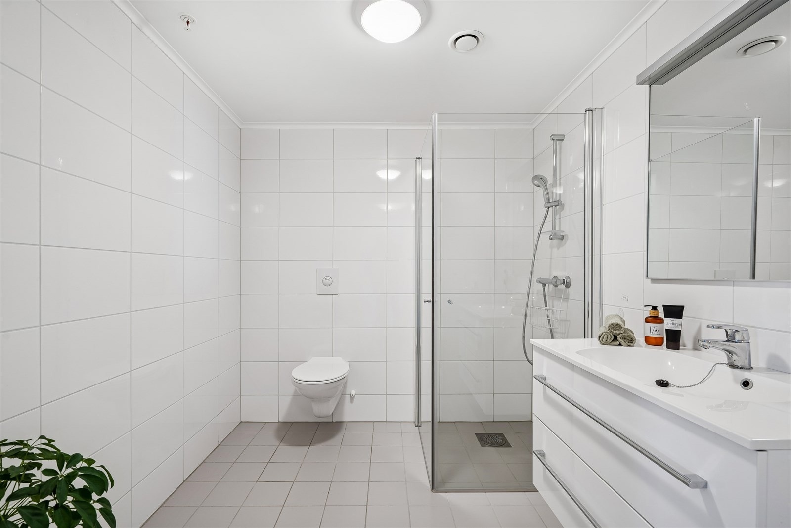 Romslig flislagt bad. Badet inneholder vegghengt wc, dusjhjørne og servant i innredning. Galleribilde