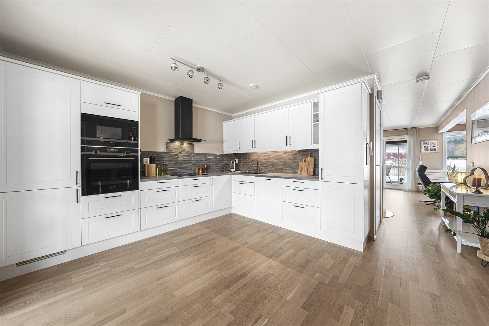 Kjøkkeninnredningen har hvite, profilerte fronter og heltre benkeplate Galleribilde