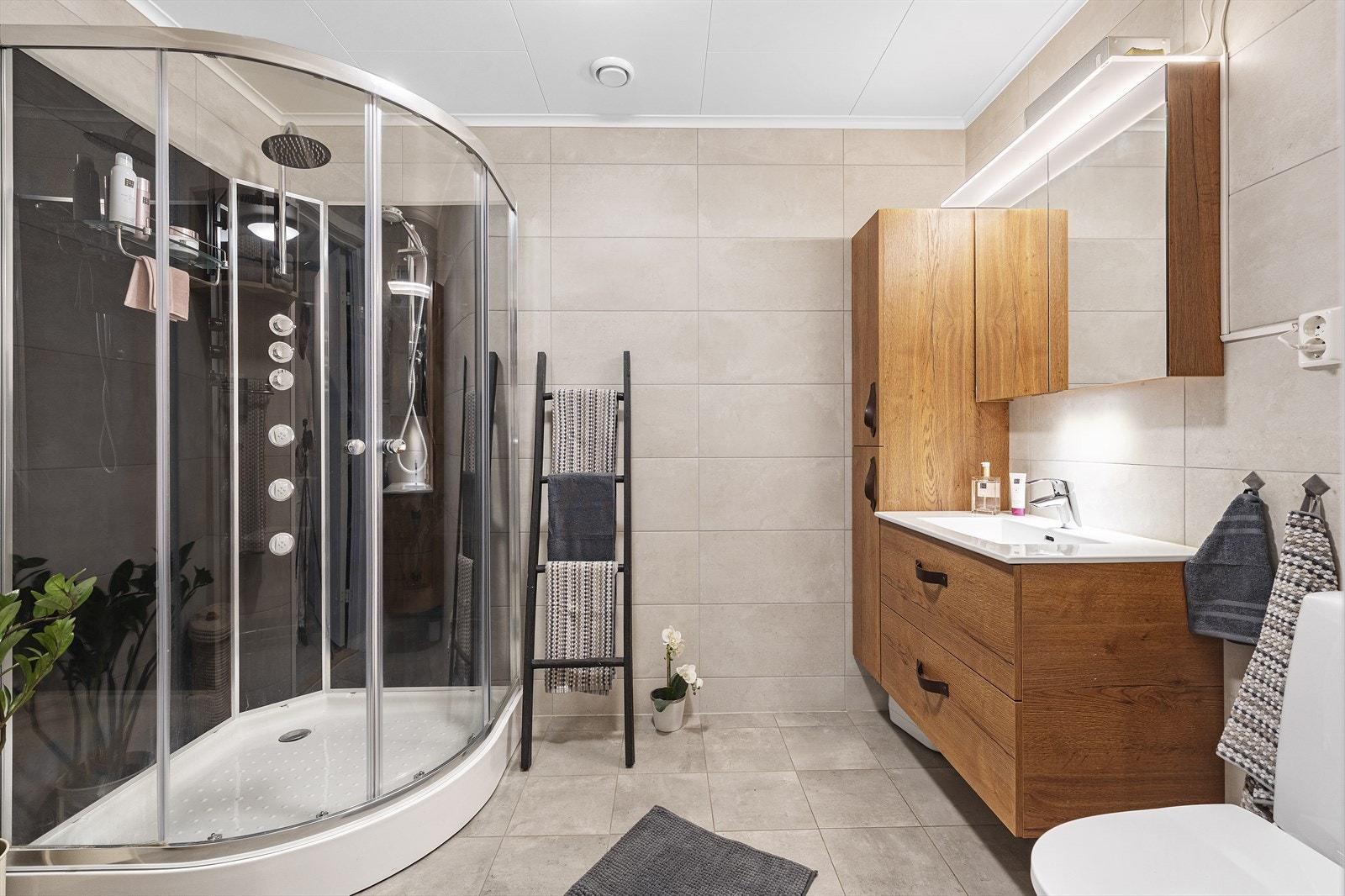 Innbydende helfliset baderom med varmekabler i gulv. Badet er innredet med heldekkende servant over skuffeinnredning, speilskap med belysning, vegghengt skap, dusjkabinett og toalett Galleribilde