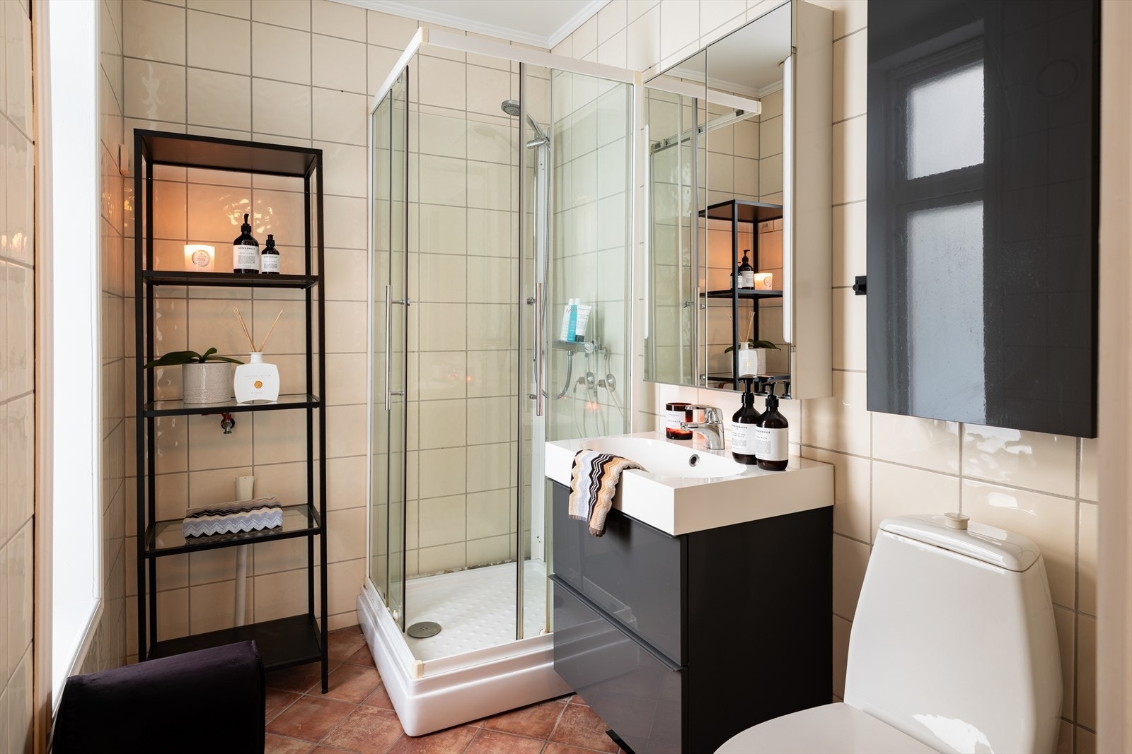 Flislagt baderom med dusjkabinett, toalett, vervant med underskap og speilskap. Galleribilde