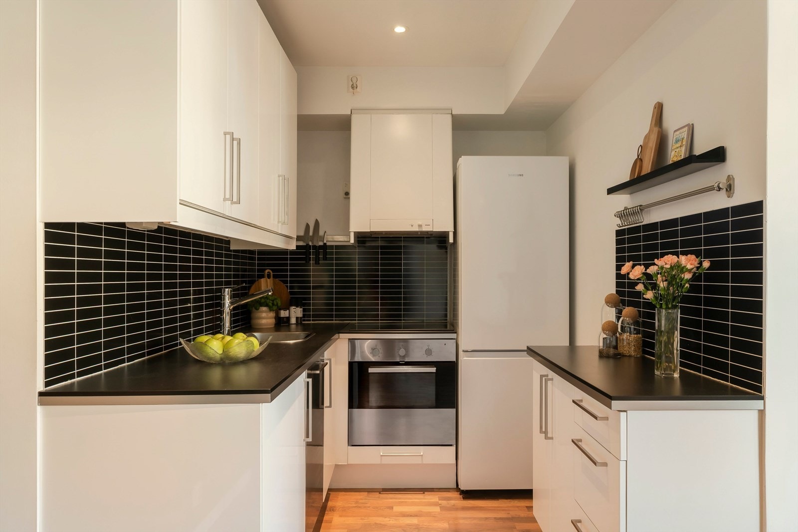 Kontrasten mellom lyse fronter og mørk benkeplate gir et moderne og ryddig uttrykk, og kjøkkenet ligger naturlig tilknyttet resten av oppholdsrommet. Galleribilde