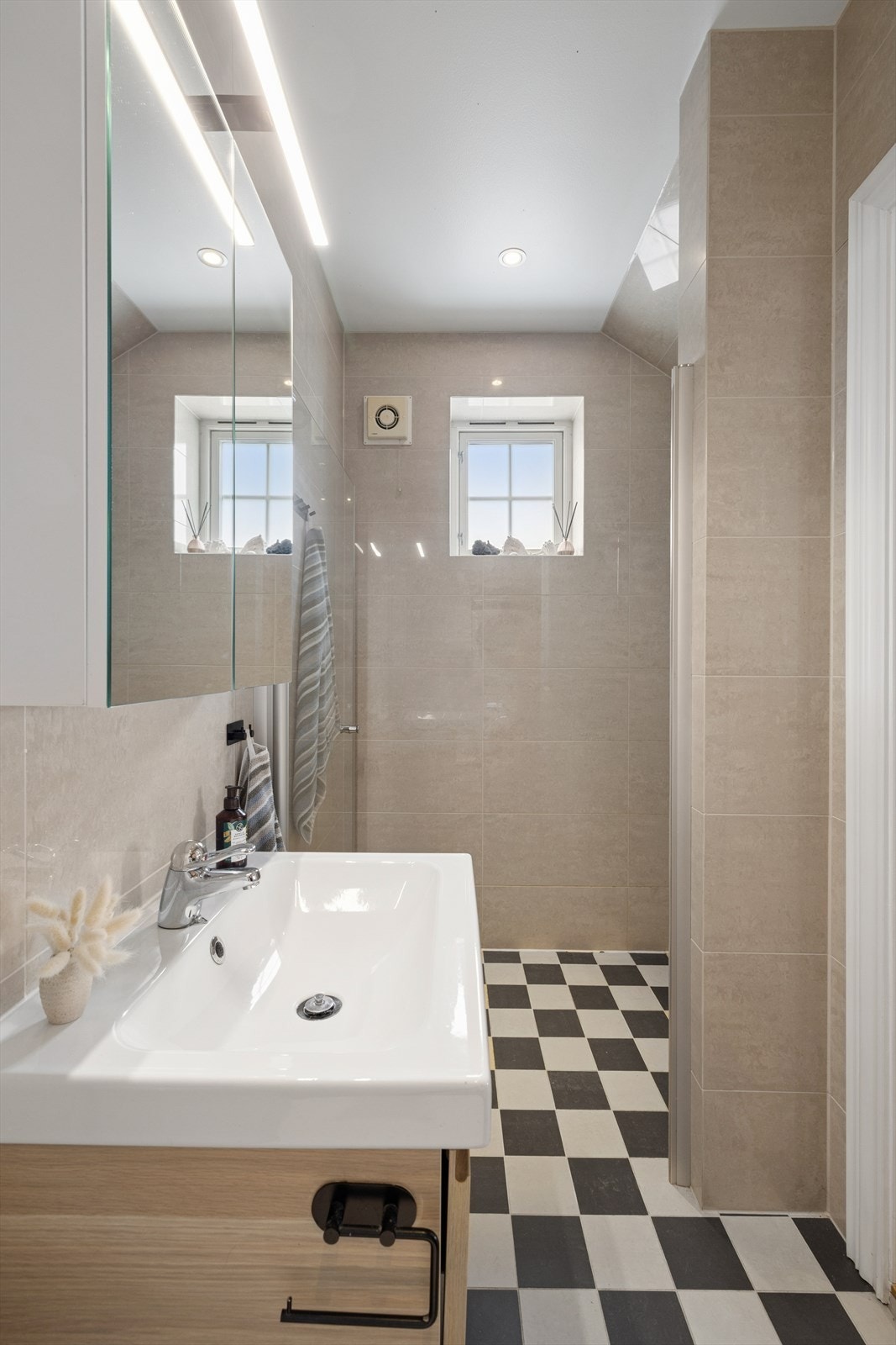 Lekker kombinasjon av klassiske sjakkrutede gulvfliser kombinert med blanke beige veggfliser som speiler seg i lyset. Galleribilde