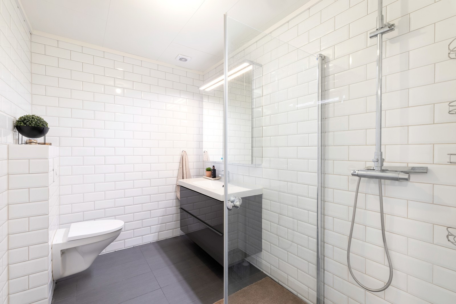 Romslig flislagt bad med vegghengt wc, servant og dusjhjørne Galleribilde