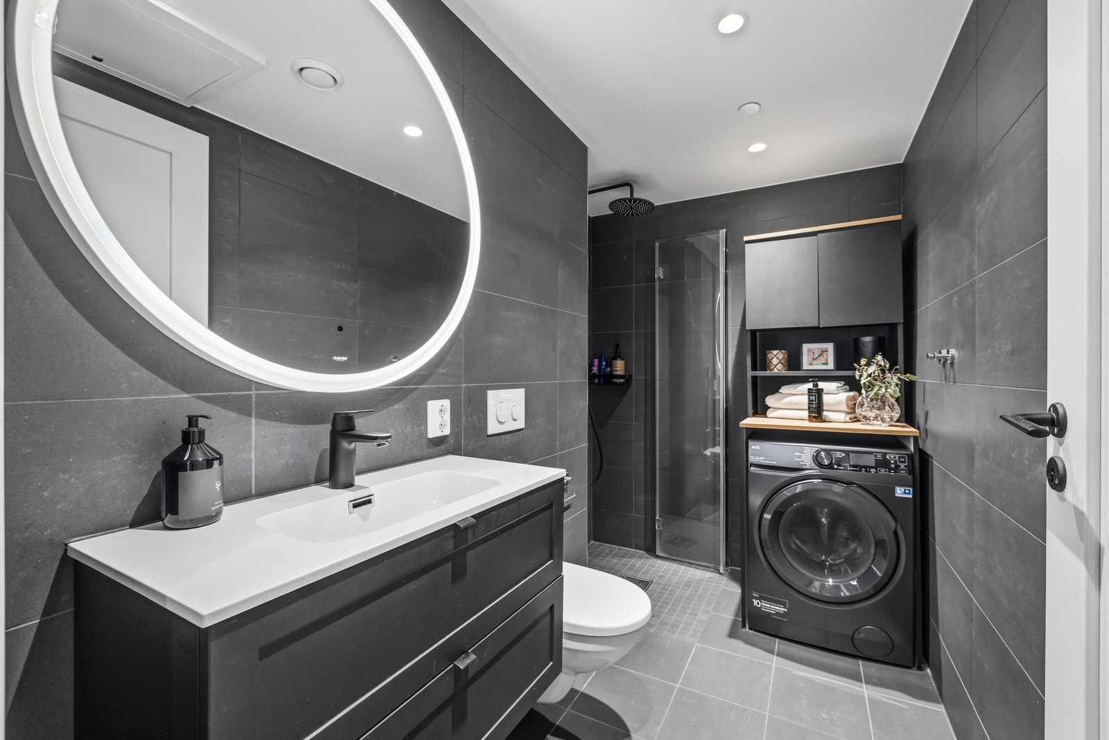 Innredningen med sorte fronter består av en romslig skuffeseksjon med heldekkende servant og stort speil med integrert belysning som gir både funksjon og atmosfære. Galleribilde