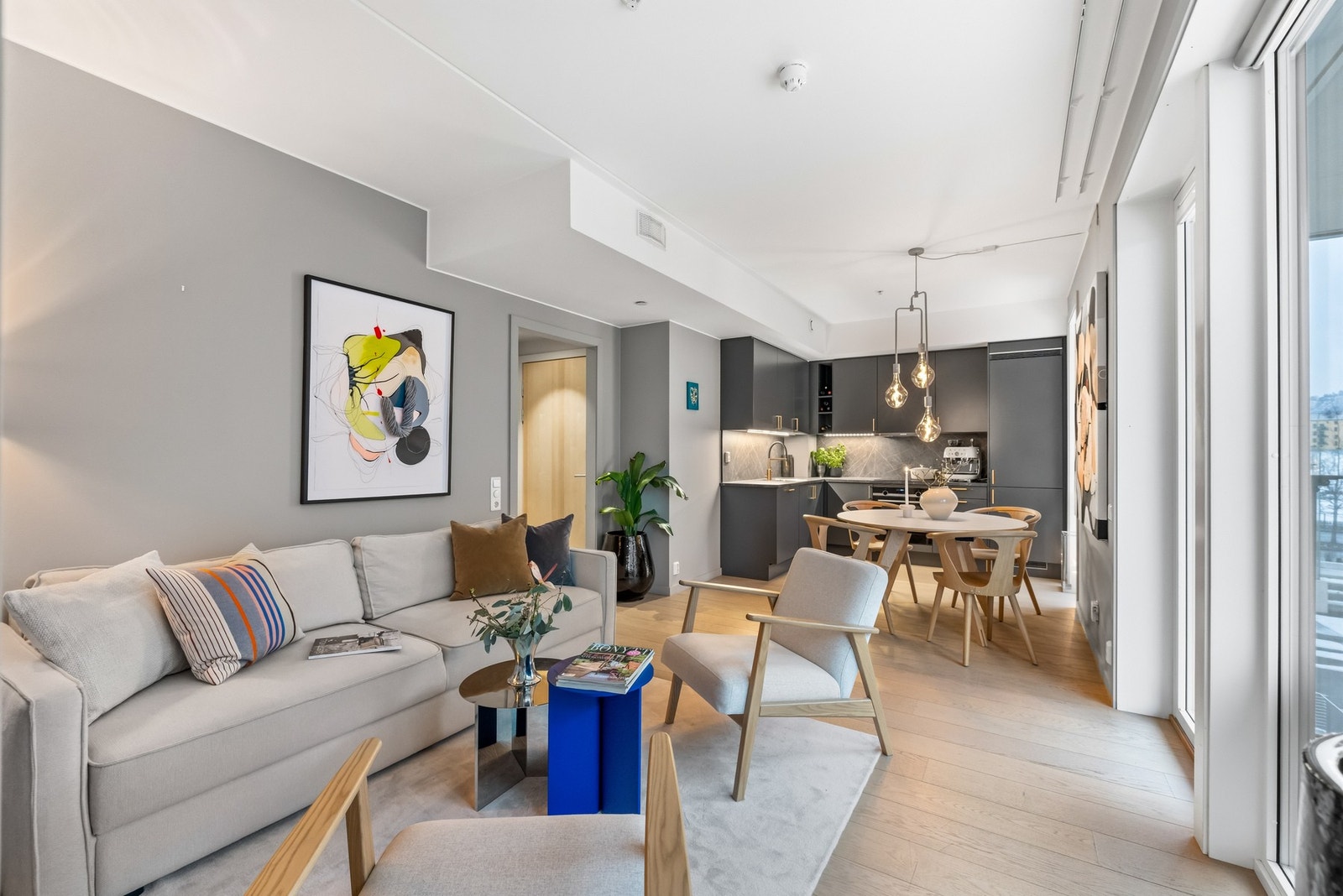 Dagslyset strømmer inn og fremhever de varme tonene i parketten og veggene, noe som gir rommet et lunt og innbydende preg. Galleribilde