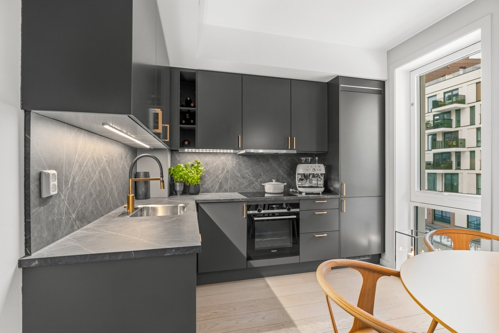 Benkeplaten i grå marmor-look laminat gir gode arbeidsflater, mens matchende veggplater og integrert belysning under overskapene sørger for både praktisk og visuelt gjennomført løsning. Galleribilde