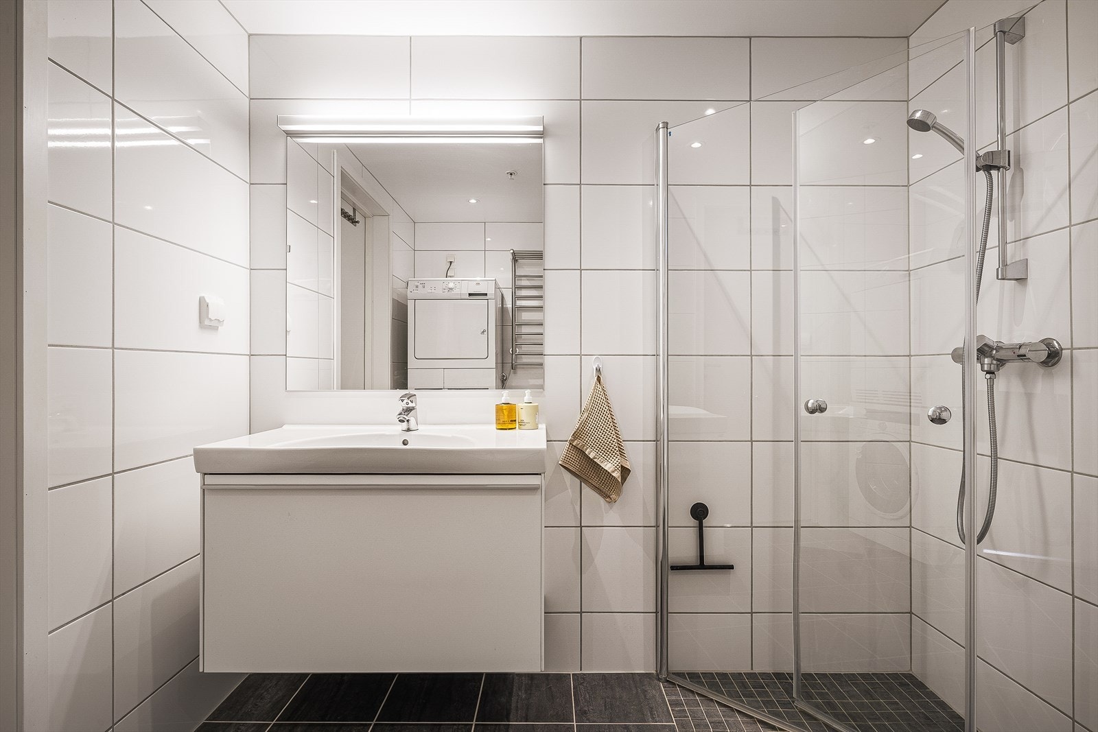 Badet har benkeskap med servant, vegghengt toalett, dusjdører og opplegg for vaskemaskin. Galleribilde