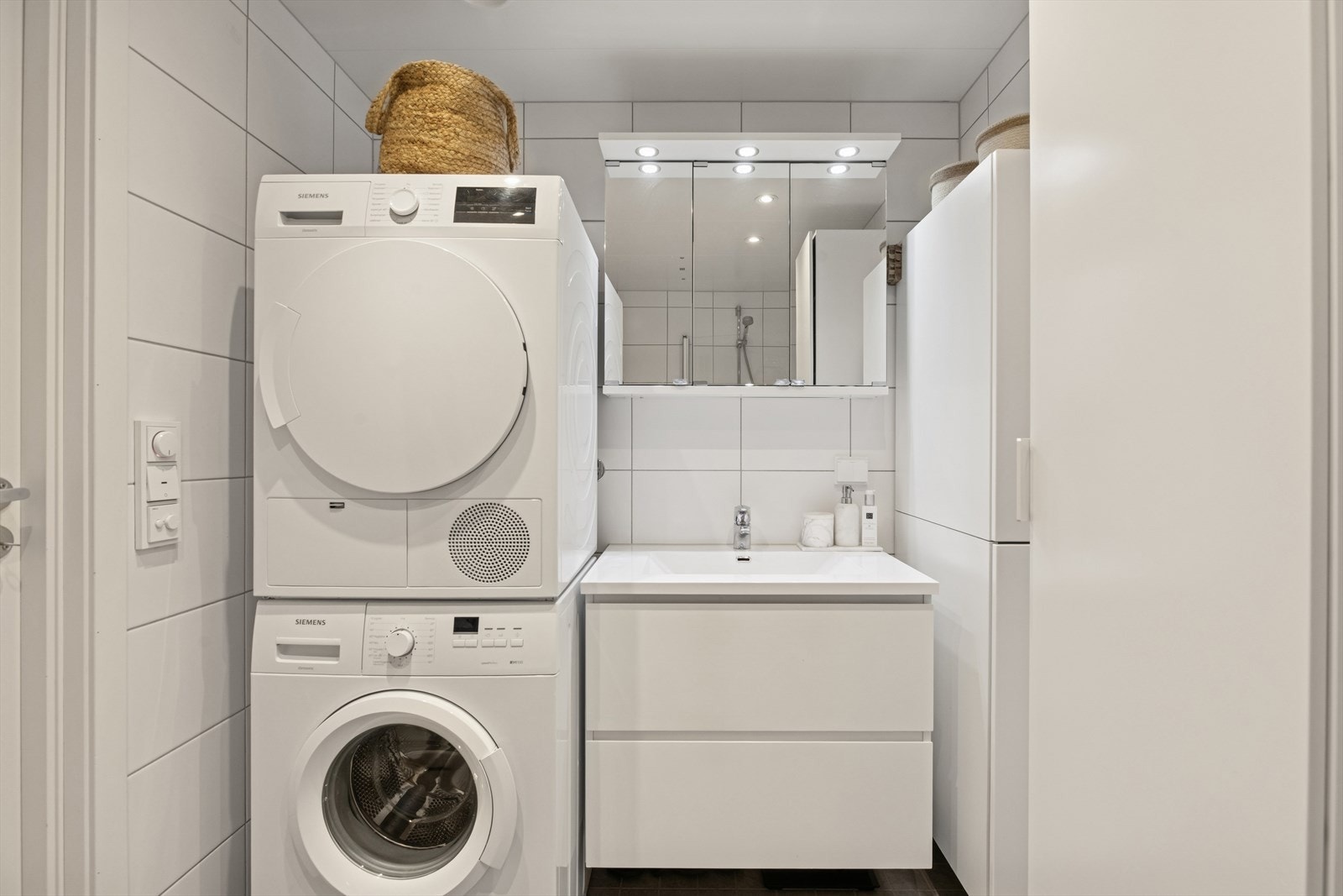 Baderomsinnredning med glatte, folierte fronter og heldekkende servant. Over servanten er det et praktisk speilskap med belysning. Galleribilde