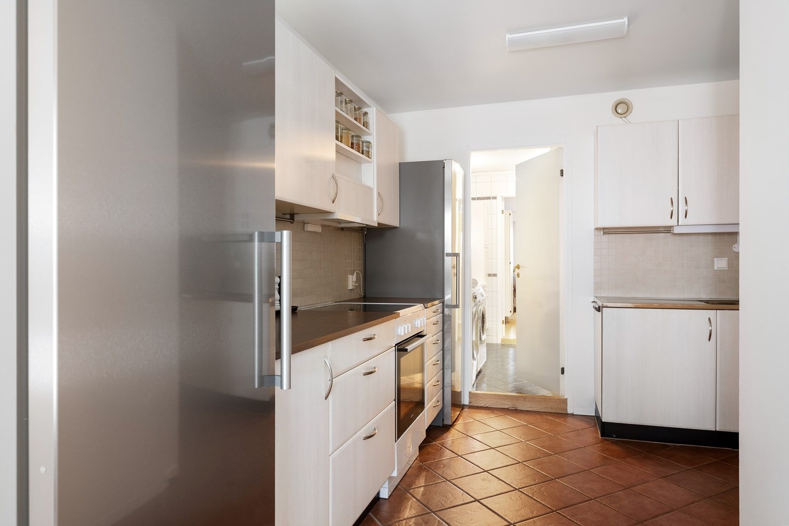 Praktisk kjøkkeninnredning med hvite, glatte fronter og god skap- og benkeplass Galleribilde