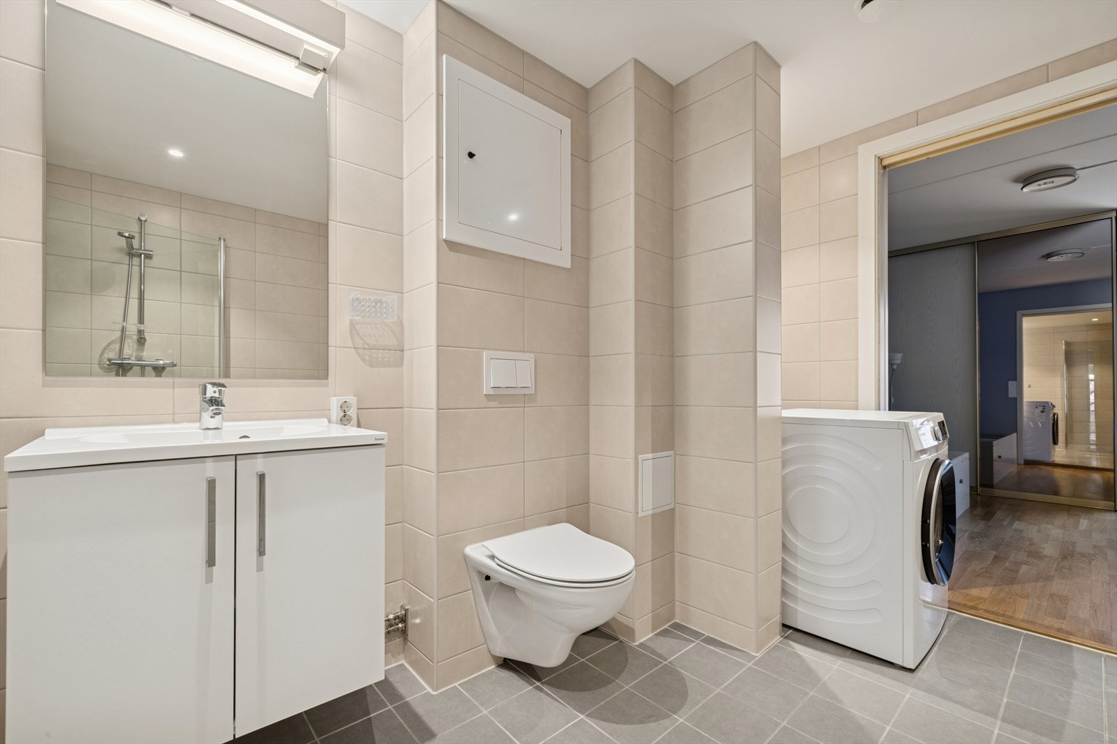 Badet er innredet med servantskap med ett-greps blandebatteri, vegghengt toalett med innebygget sisterne, veggspeil, lysarmatur, avskjermet dusjhjørne med glass, blandebatteri og dusjgarnityr. Galleribilde