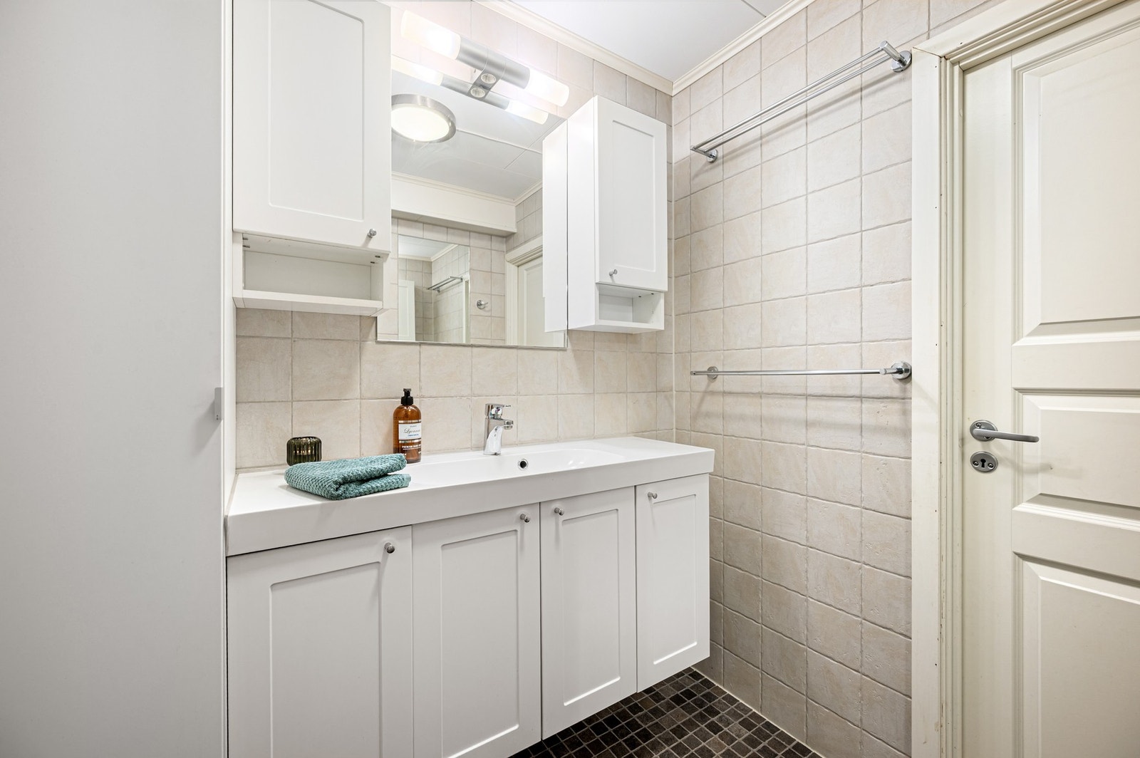 Praktisk baderomsinnredning med vegghengt servant, gode oppbevaringsløsninger og speil med belysning. Galleribilde