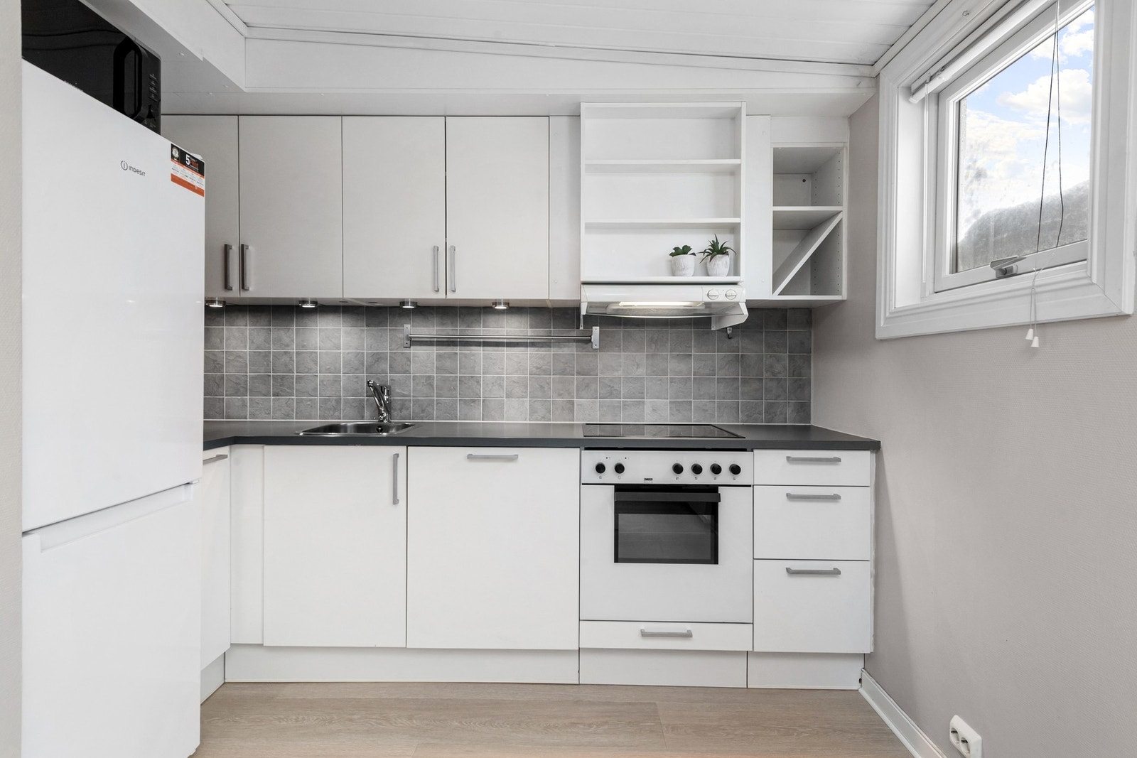 Lys kjøkkeninredning med integrert komfyr, platetopp, oppvaskmaskin. Galleribilde