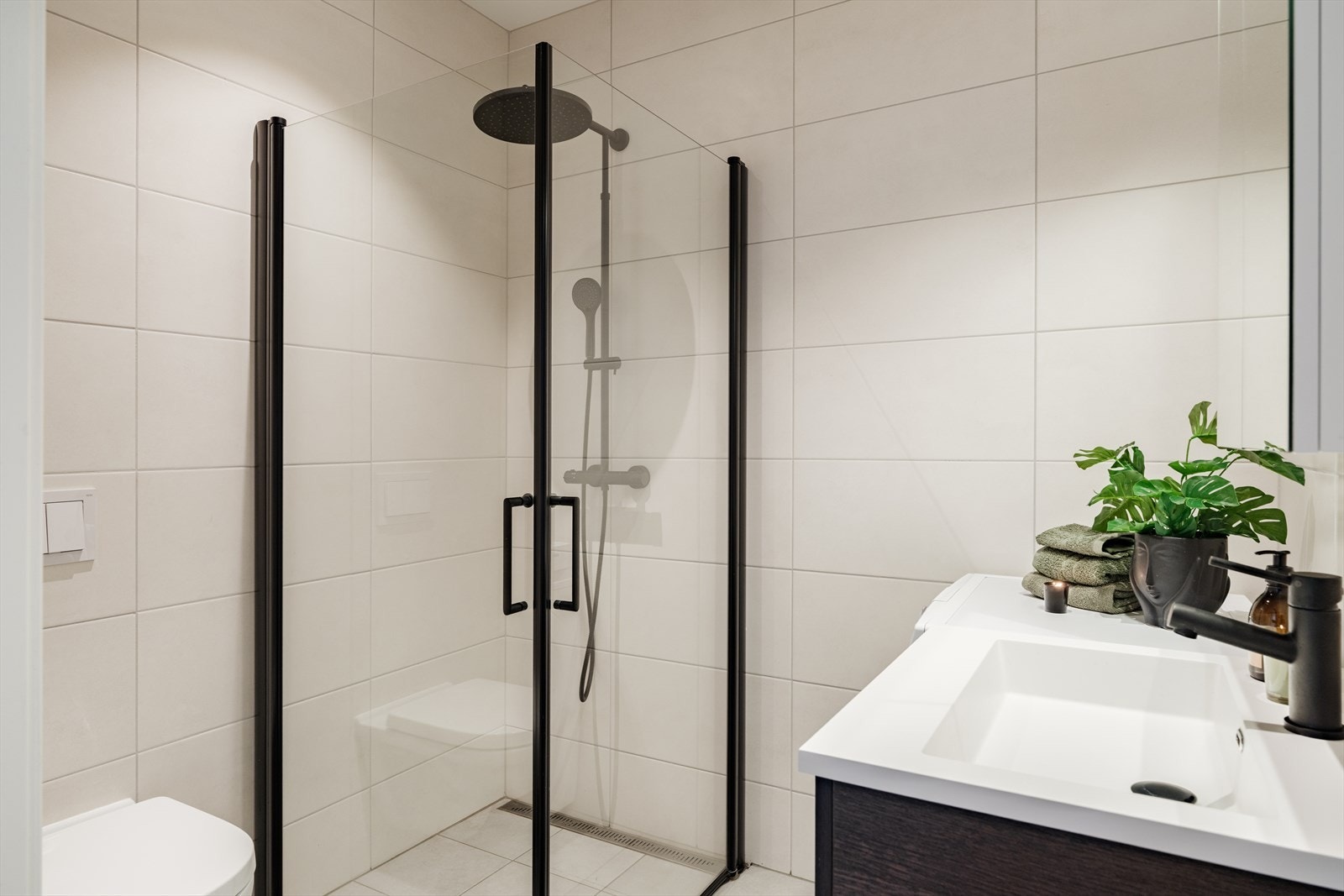 Komplett og moderne. Walk-in dusj, servant og toalett i stilrent uttrykk. Hvite fliser og sort armatur gir tidløs eleganse. Galleribilde