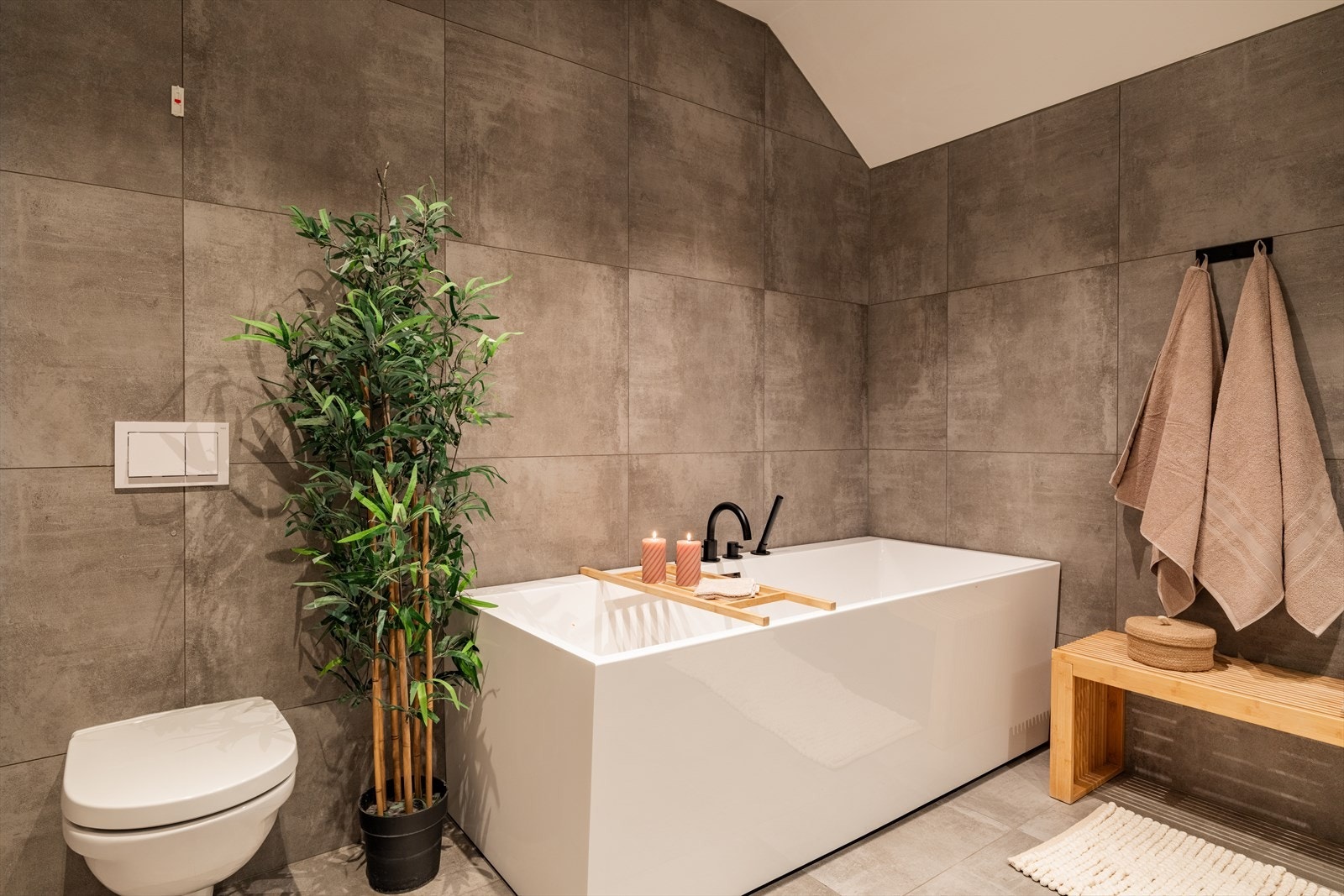 Spa-følelse hjemme. Romslig familiebad med frittstående badekar, walk-in dusj med svart innramming og vaskemaskin/tørketrommel diskret plassert. Store fliser i varm gråtone skaper ro og eleganse. Galleribilde