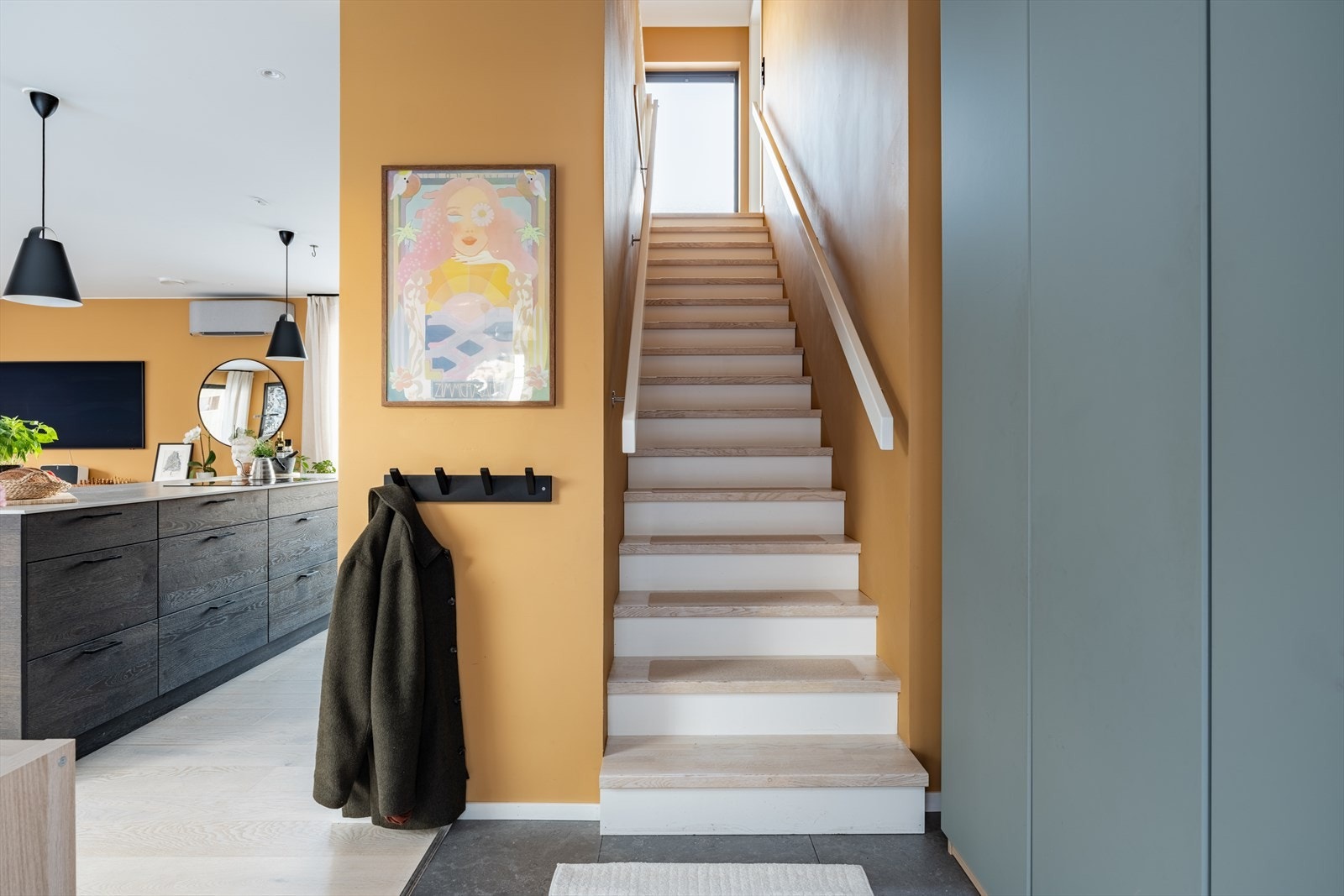 Gjennomtenkt fra første steg. Entréen ønsker velkommen med varme farger og smarte løsninger. Trappen opp til 2. etasje er lys og innbydende. Sennepsgule (Burnt Ochre - Jotun 2023) vegger og en lys trapp opp til vinduer med utsikt helt mot SNÖ. Galleribilde