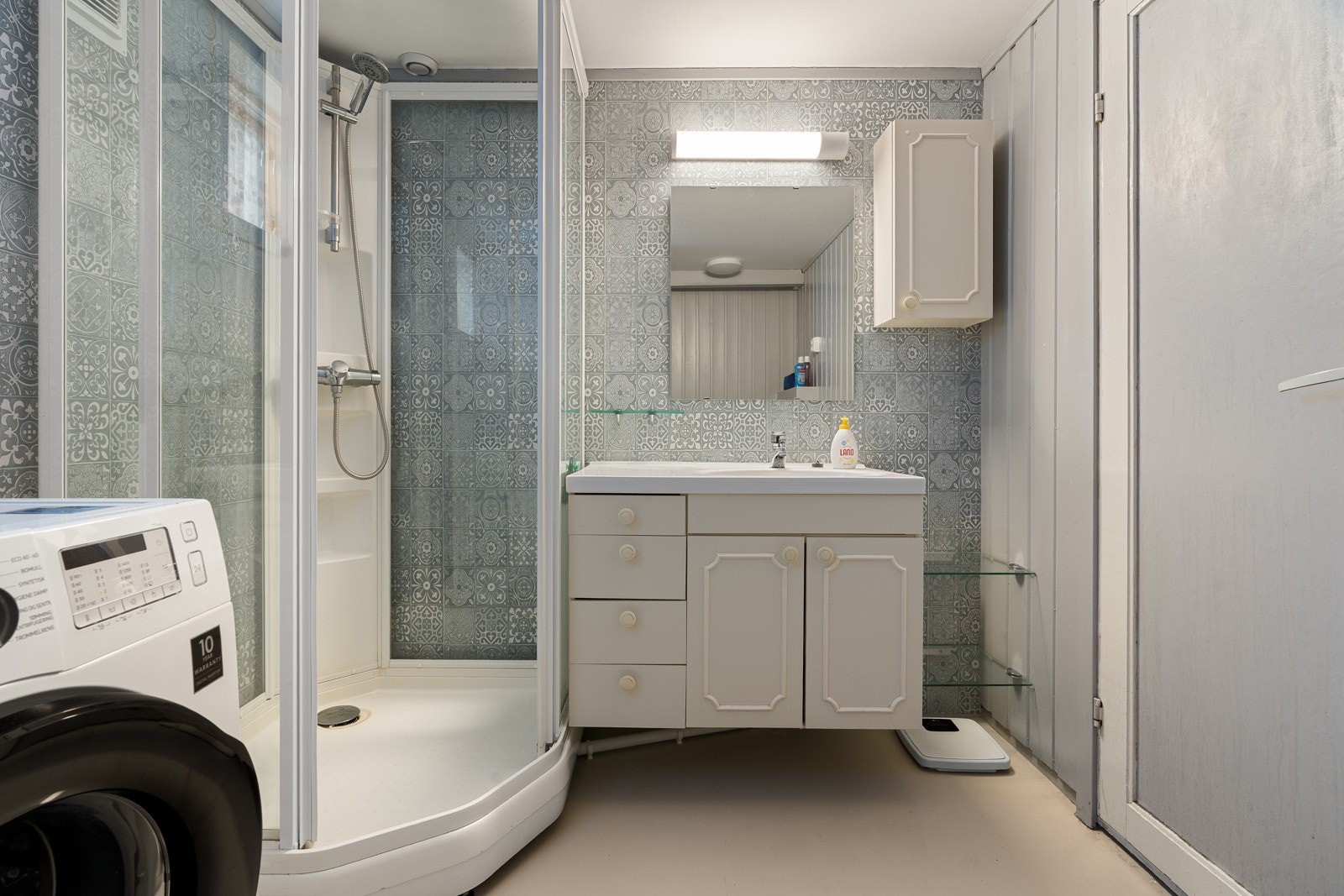 Bad/wc i sokkel med lys baderomsinnredning med servant, speil og dusjkabinett. Galleribilde