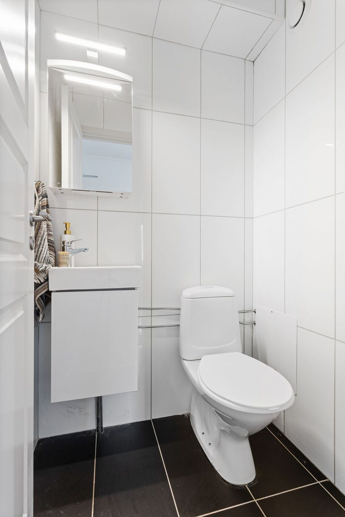 Lyst og stilrent toalettrom med fliser, moderne servantinnredning og mekanisk avtrekk - et praktisk og velholdt rom med tidløst uttrykk Galleribilde