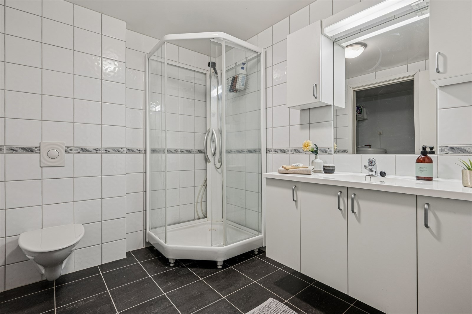 Badet er av god størrelse og er tidløst innredet med grå fliser på gulvet og hvite fliser på vegg. I gulvet har man også varmekabler for ekstra komfort. Galleribilde