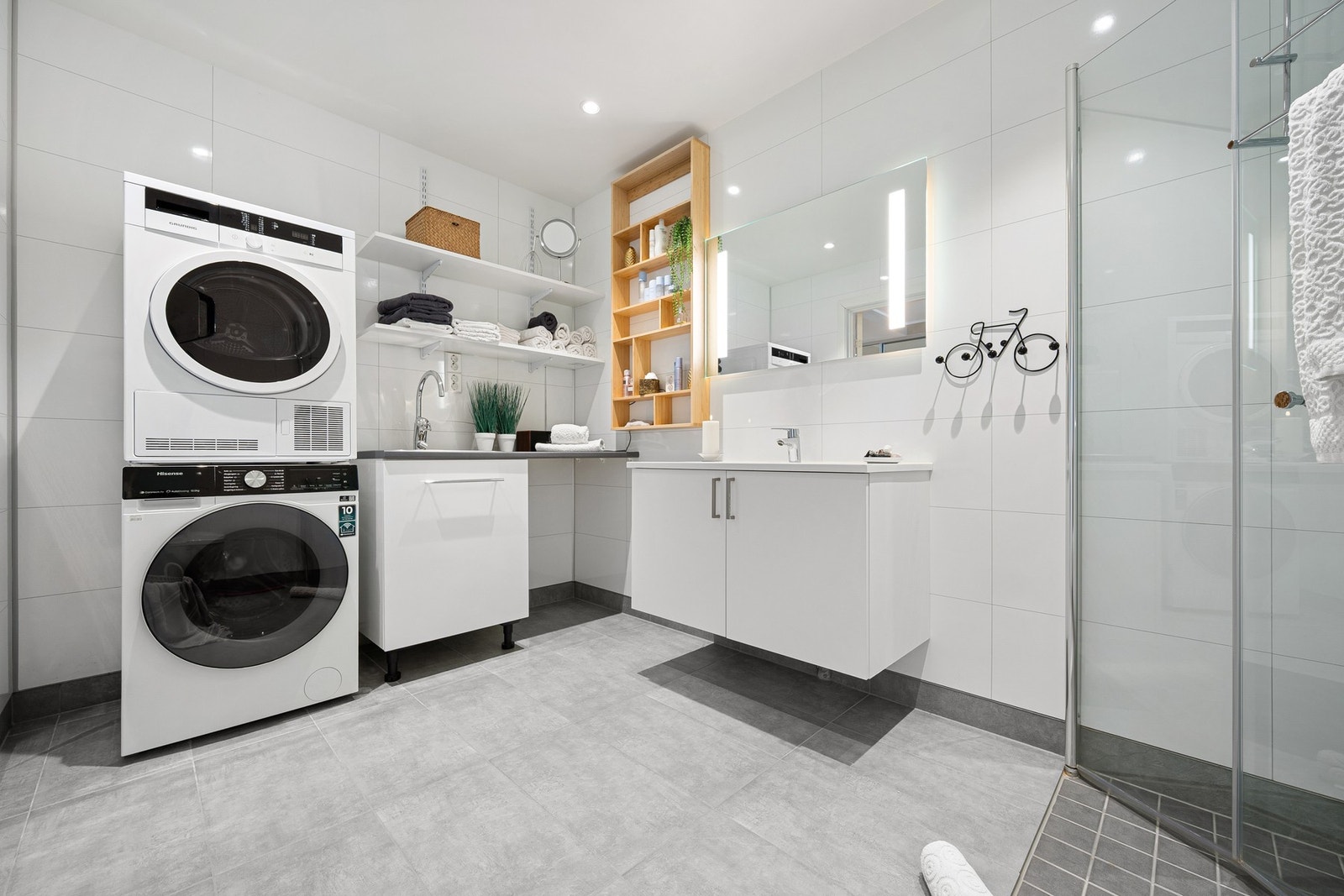 Rommet er kombinert bad og vaskerom, som inneholder servantinnredning, dusjhjørne, toalett og opplegg for vaskemaskin Galleribilde